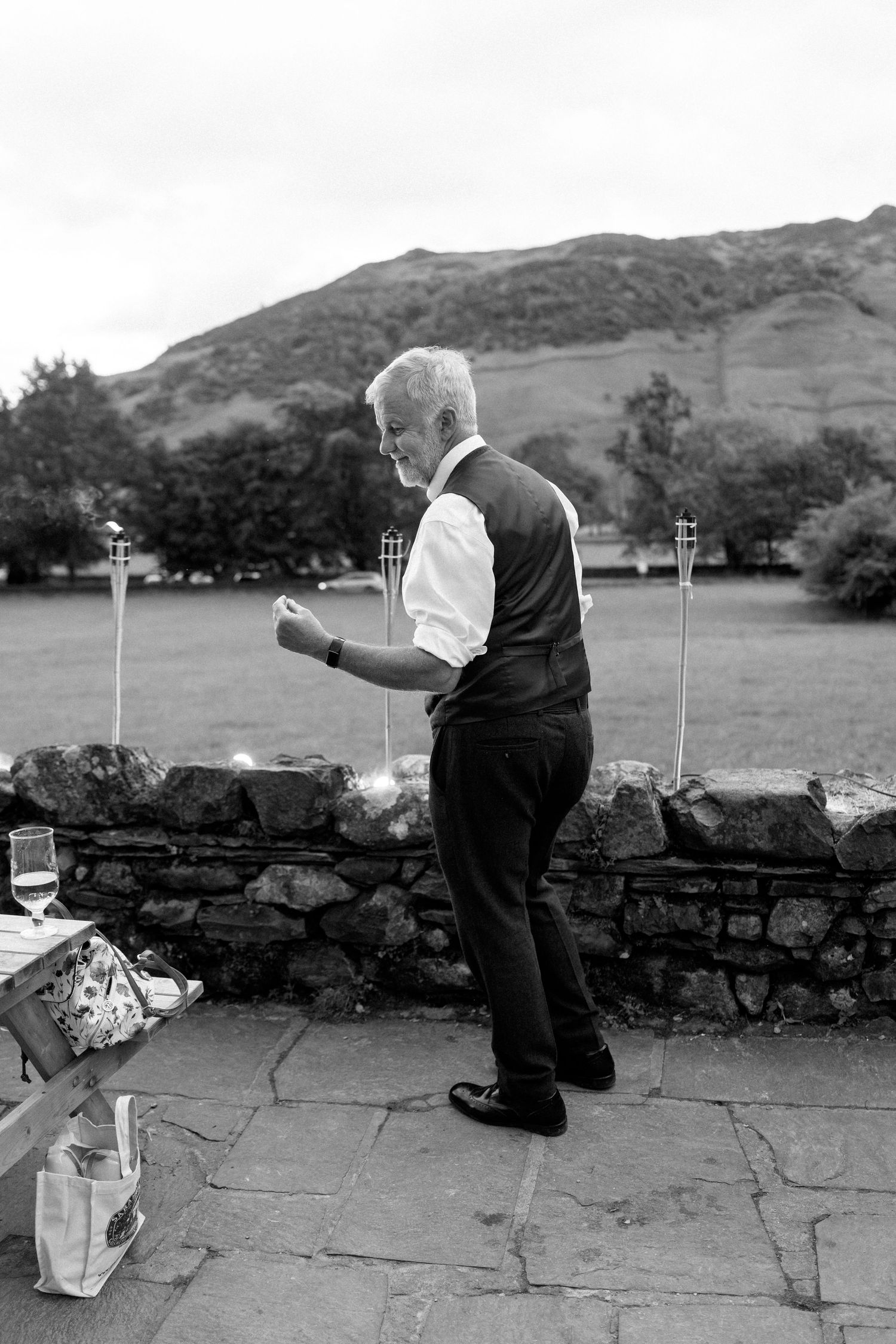 Black and white photo of couple dancing on stone patio with mountains in background.