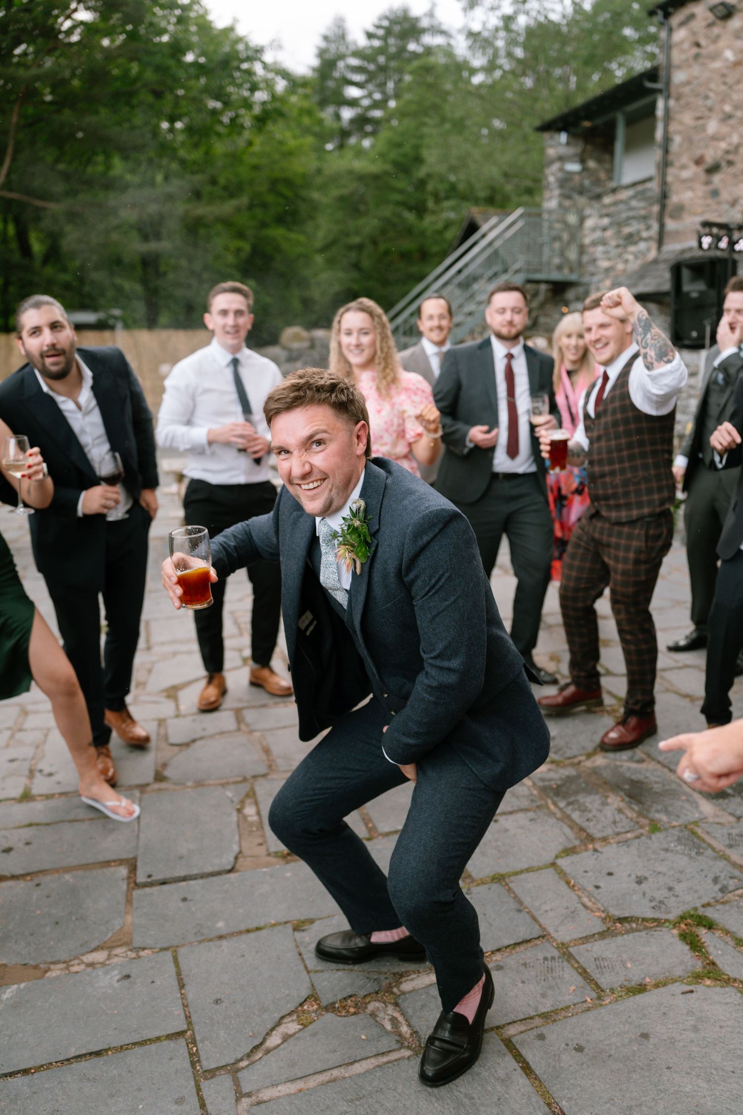 Wedding guest strikes a playful pose on stone patio during outdoor reception celebration.