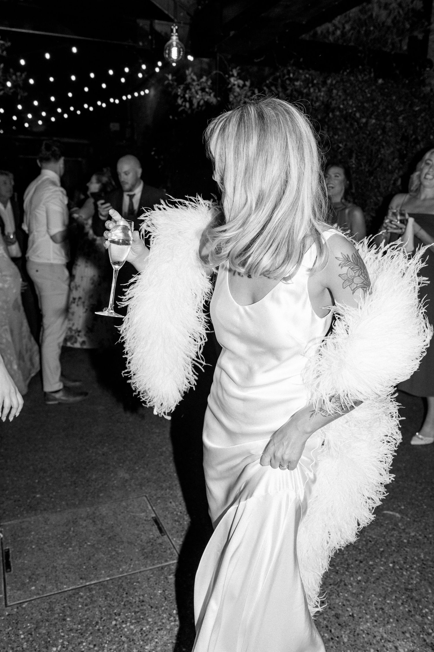 A bride wearing white feather sleeves dances at an evening reception.