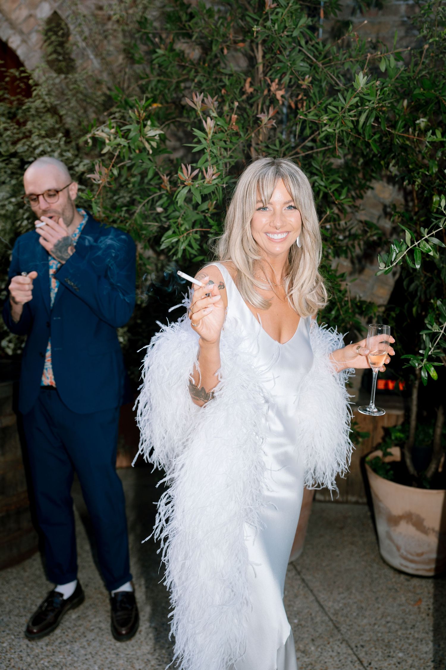 A bride in a feathered white dress dances joyfully outdoors under string lights at night.