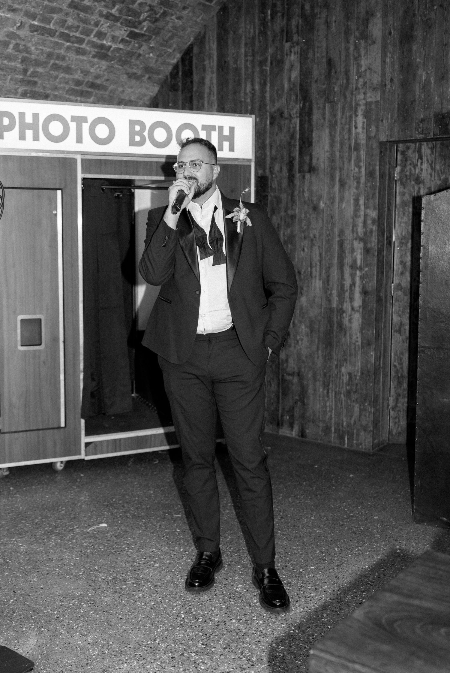 Black and white photo of a person in a suit standing near a photo booth at an event.