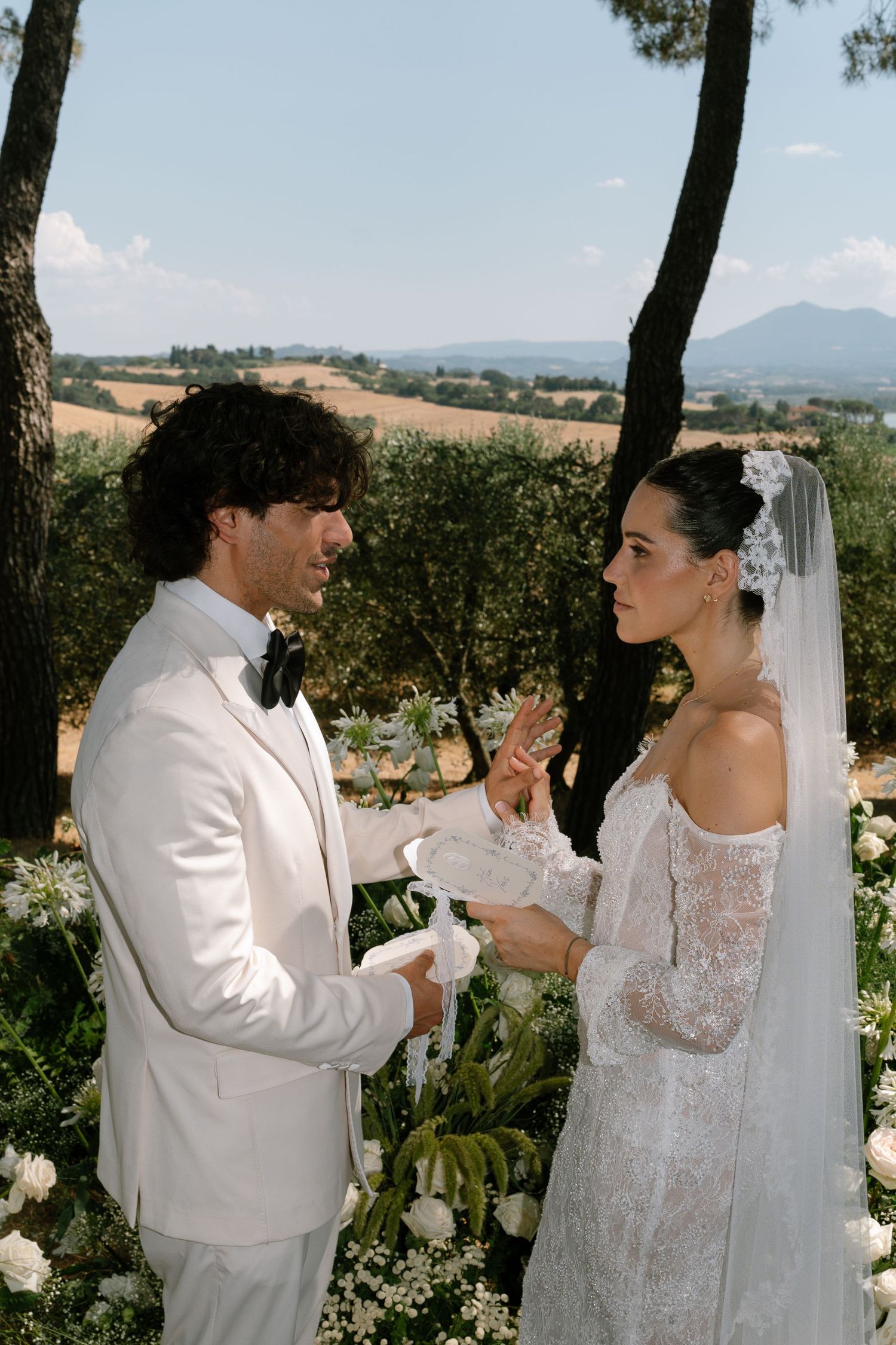 A couple in white formal attire sharing a drink together in a scenic outdoor setting.