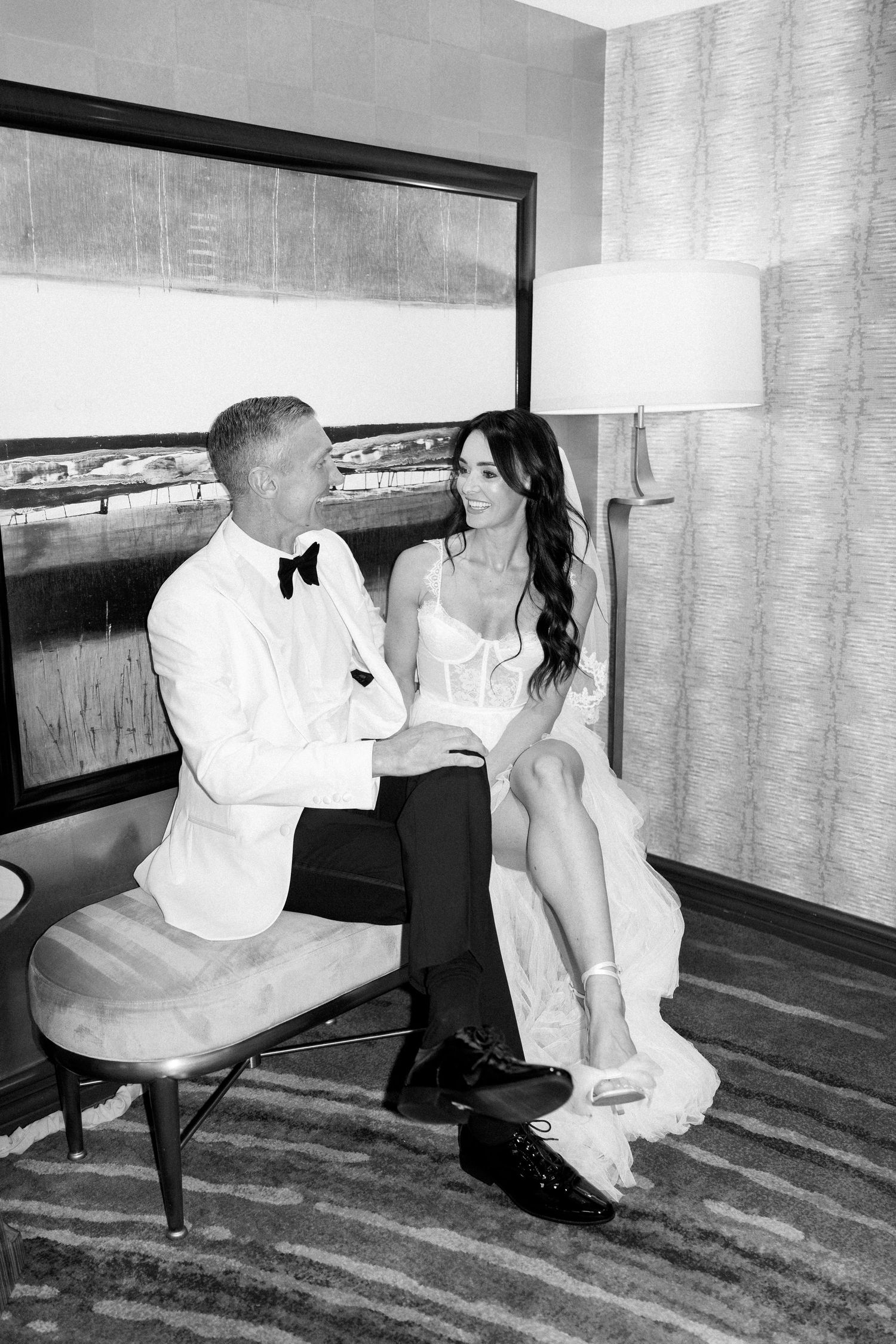 Couple in formal wedding attire sharing playful moments in a hotel room with blue carpeting.