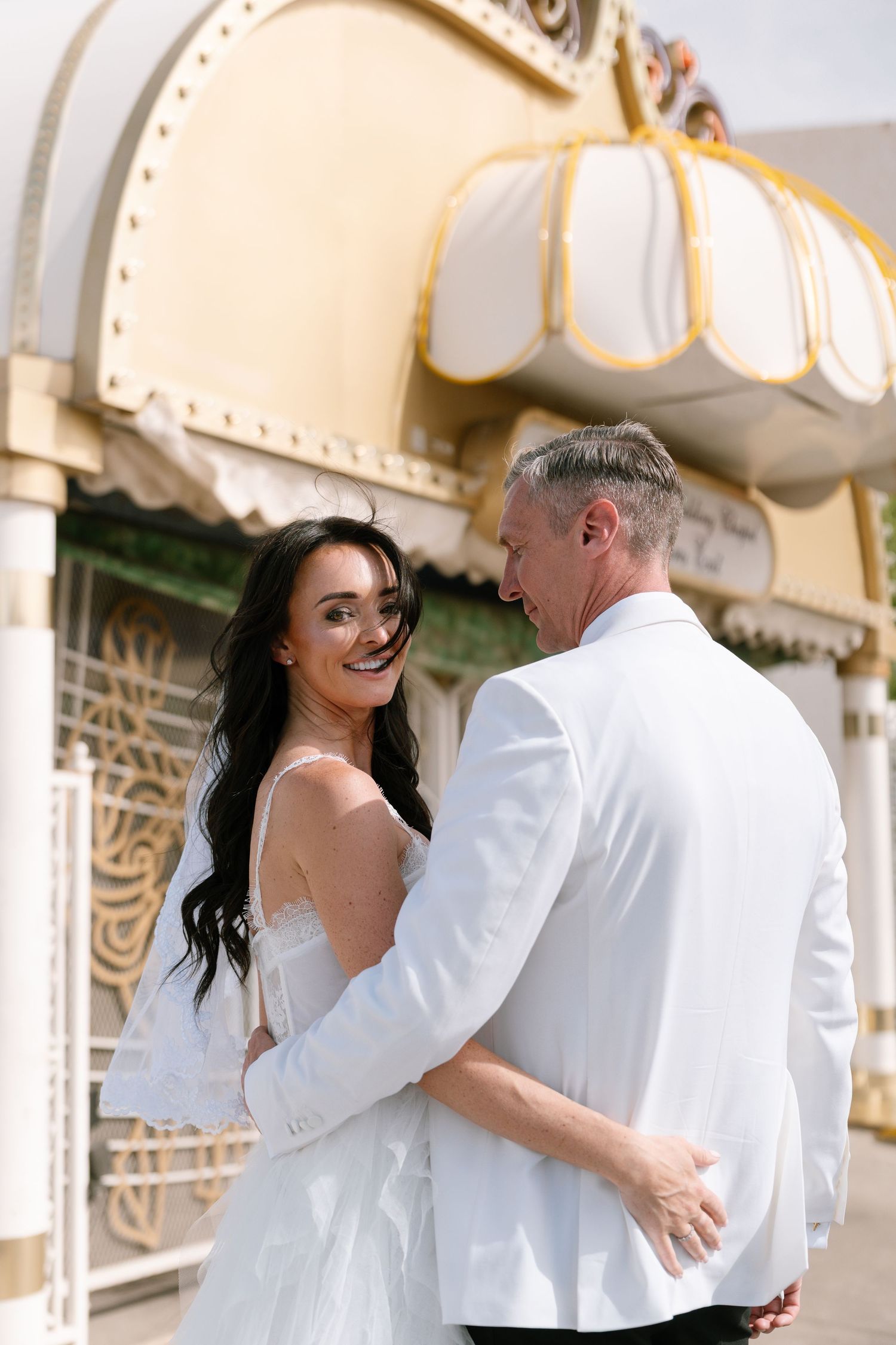 Romantic couple embraces in an elegant white interior with ornate decor and lighting.