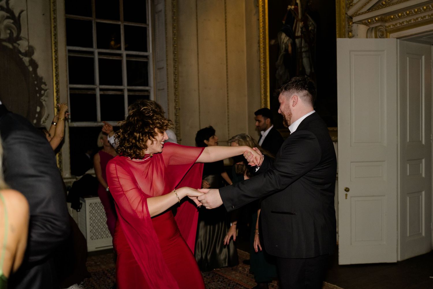 Guests in formal attire dancing energetically at an elegant wedding reception with ornate decor.