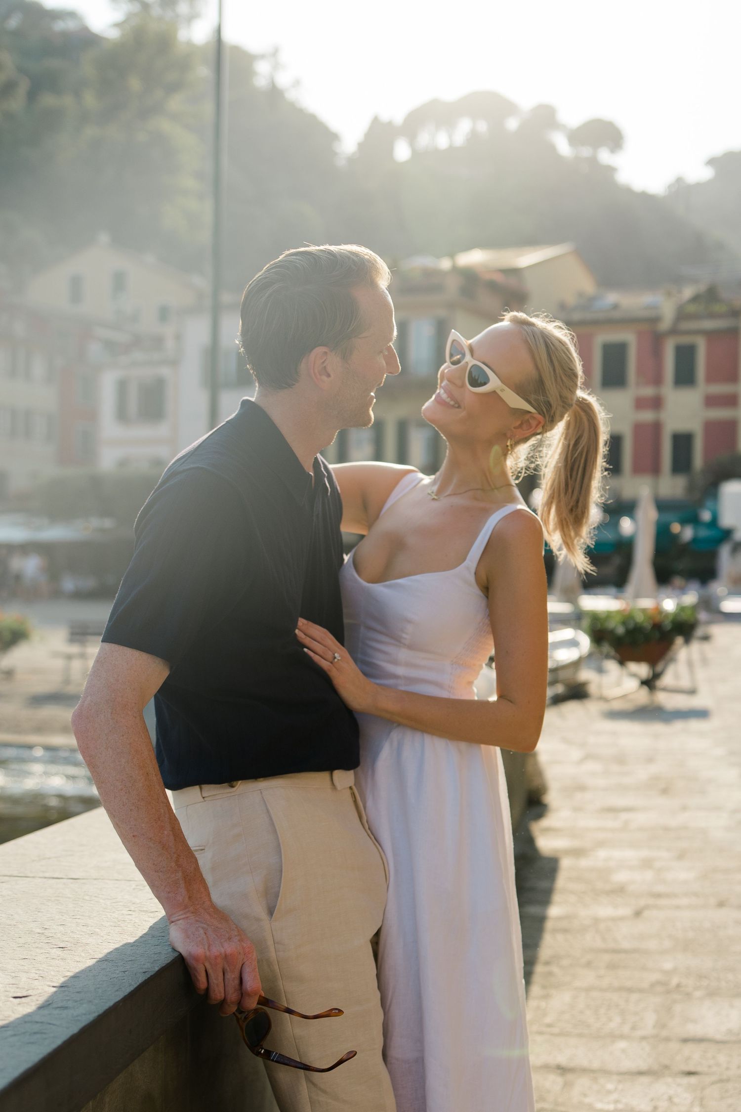 Couple sharing a romantic moment on a sunlit waterfront promenade in Portofino, Italy.