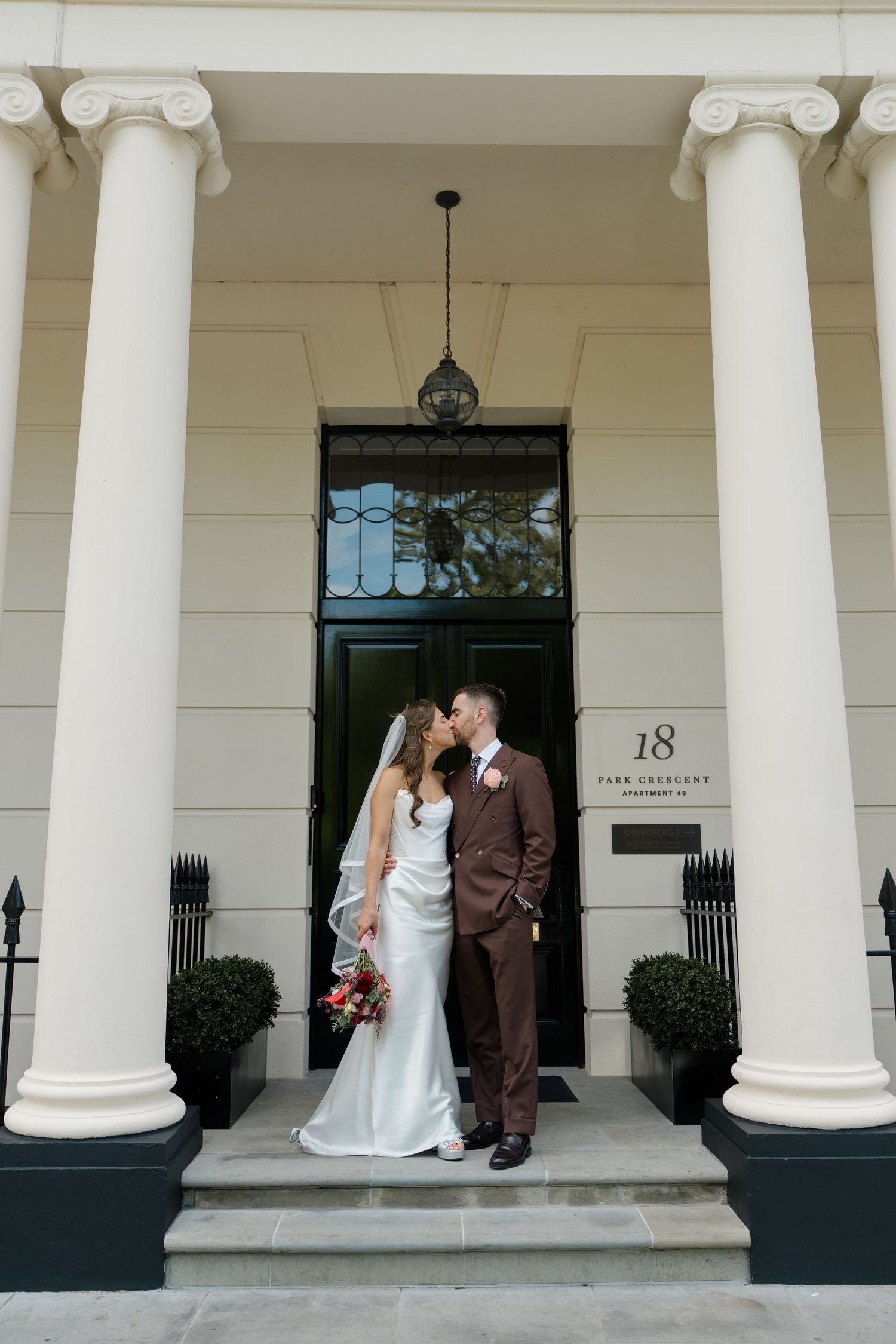 Bride and groom kissing on steps of elegant Georgian building with white columns at 18 Park Crescent London.