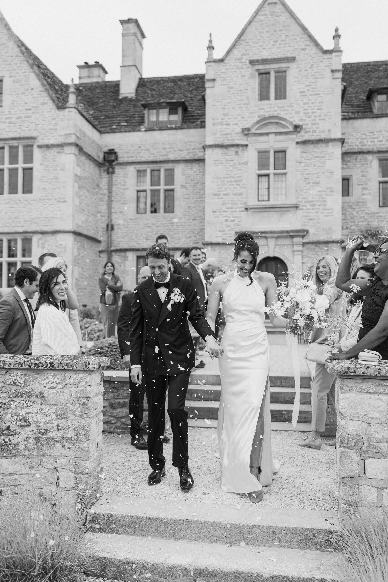 Black and white photo of bride and groom descending stone steps through confetti at historic manor wedding.