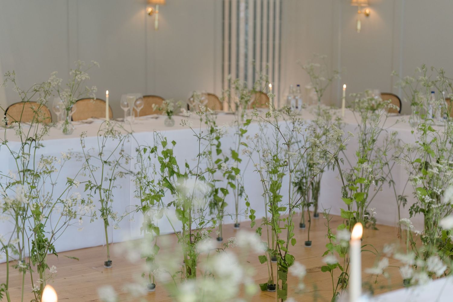 Elegant wedding reception room with tall greenery centerpieces, white taper candles, and draped ceiling decor.