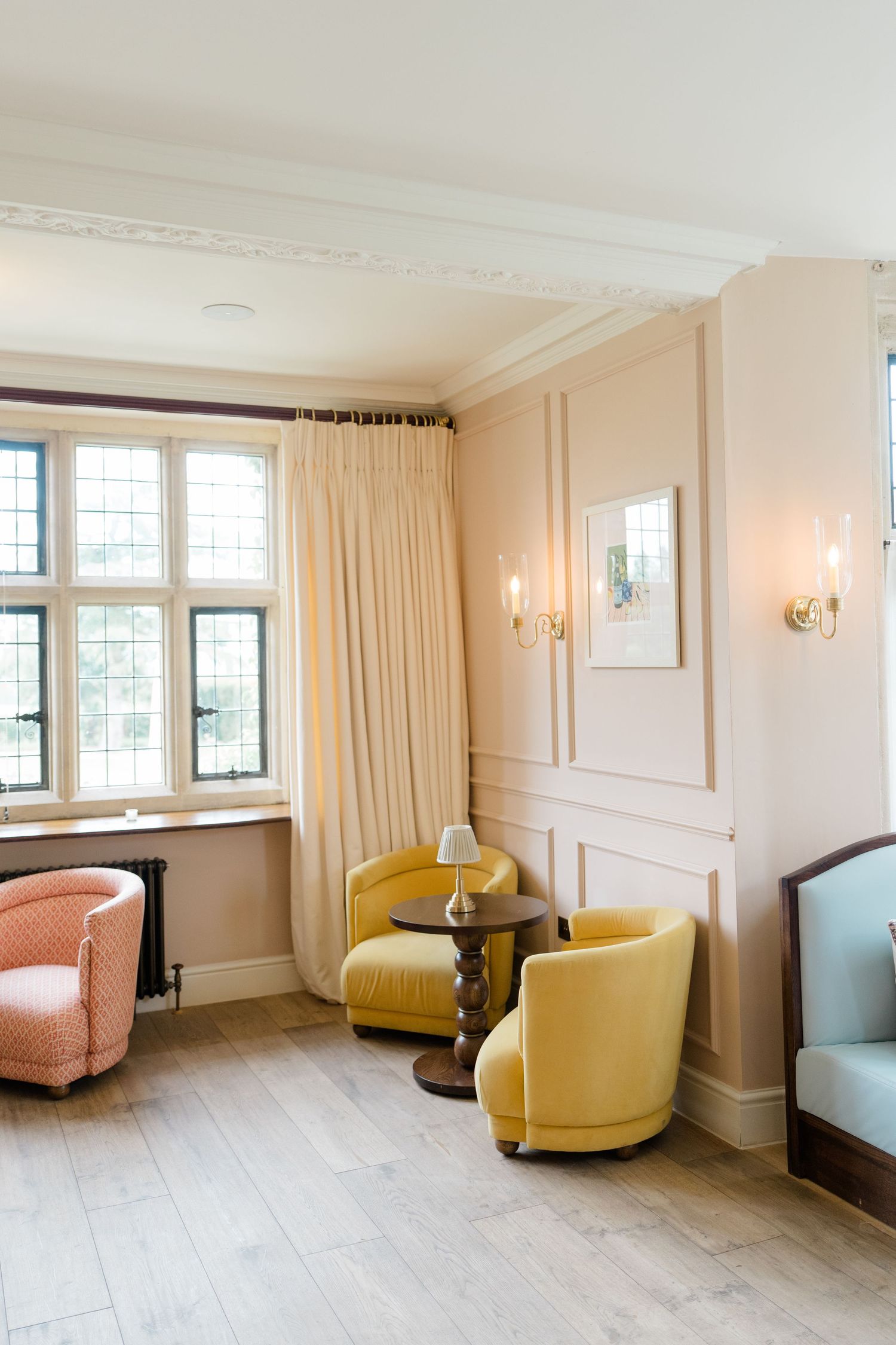 Elegant hotel lounge with yellow velvet armchairs, pink walls, ornate crown molding, and leaded windows.