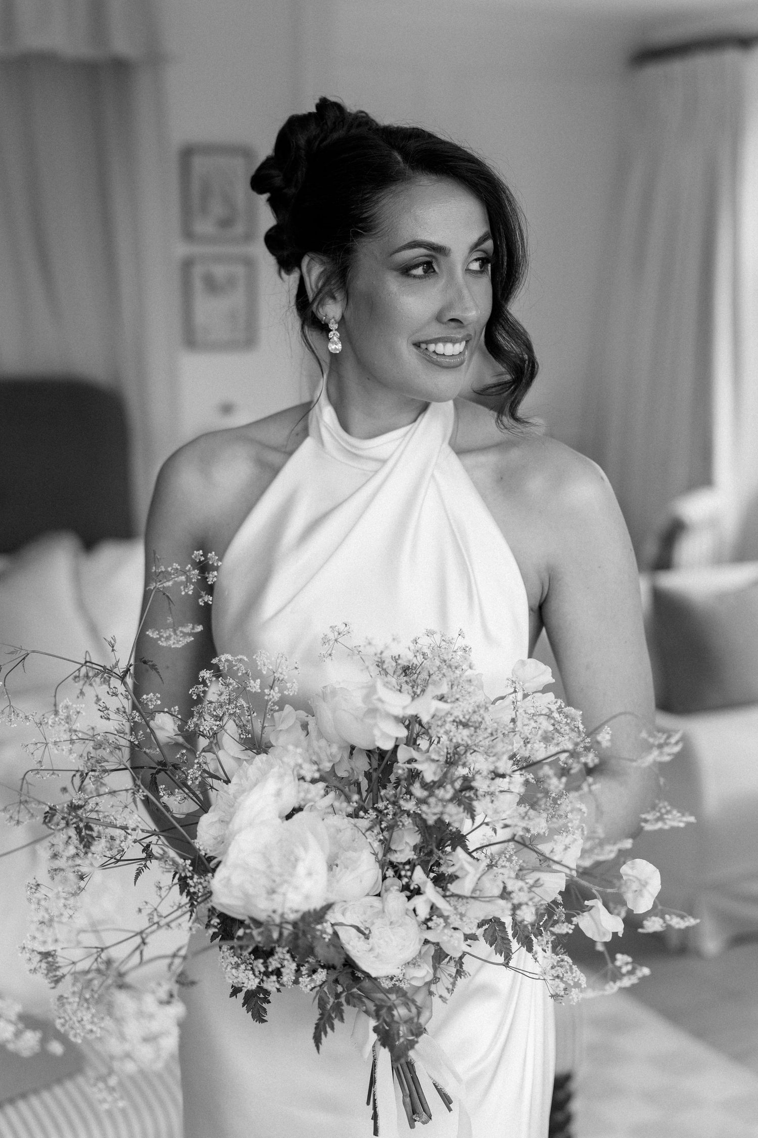 Black and white portrait of bride in halter gown holding lush white bouquet with soft smile.