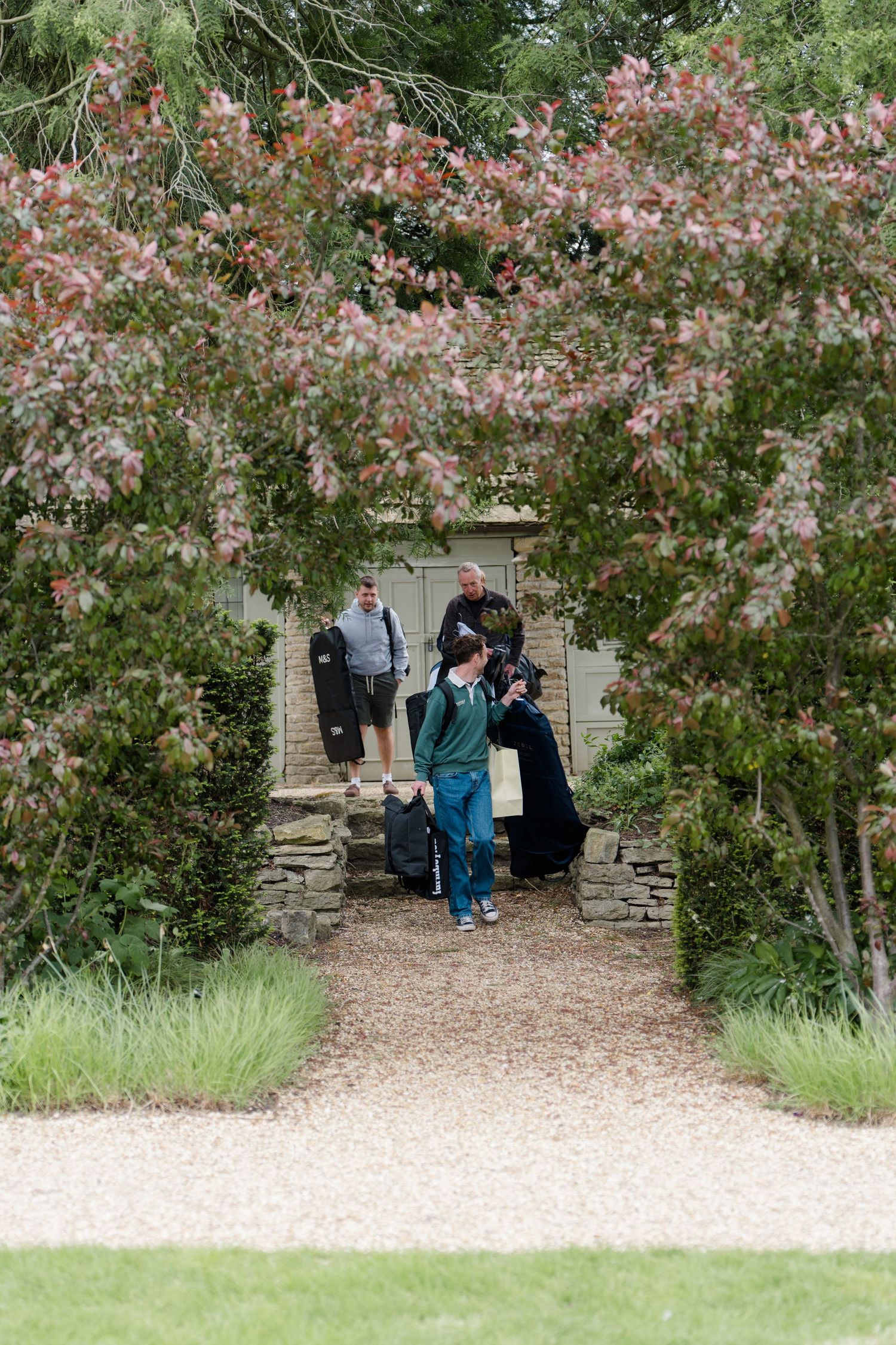 Guests walking through a stone archway framed by trees along a gravel garden path.