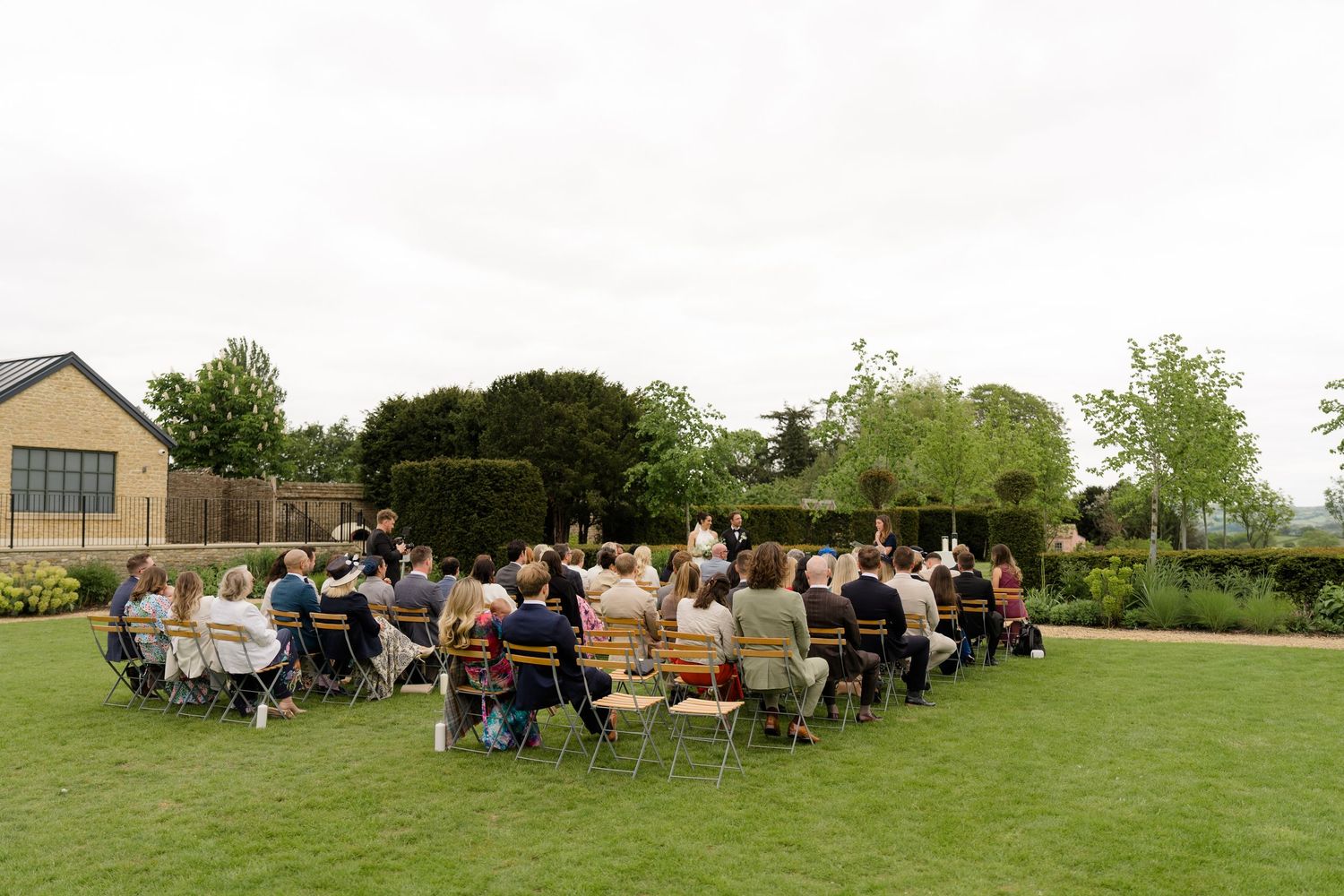Wedding guests seated on colorful chairs during an outdoor garden ceremony on a lush green lawn.