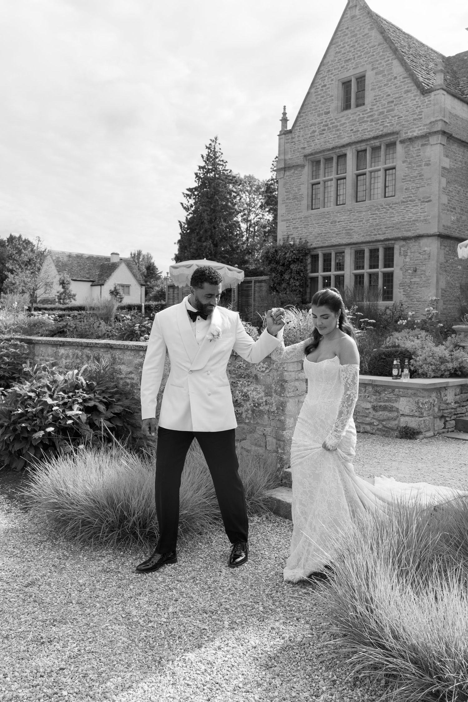 Bride and groom dancing elegantly outside a stone manor in black and white wedding photo.