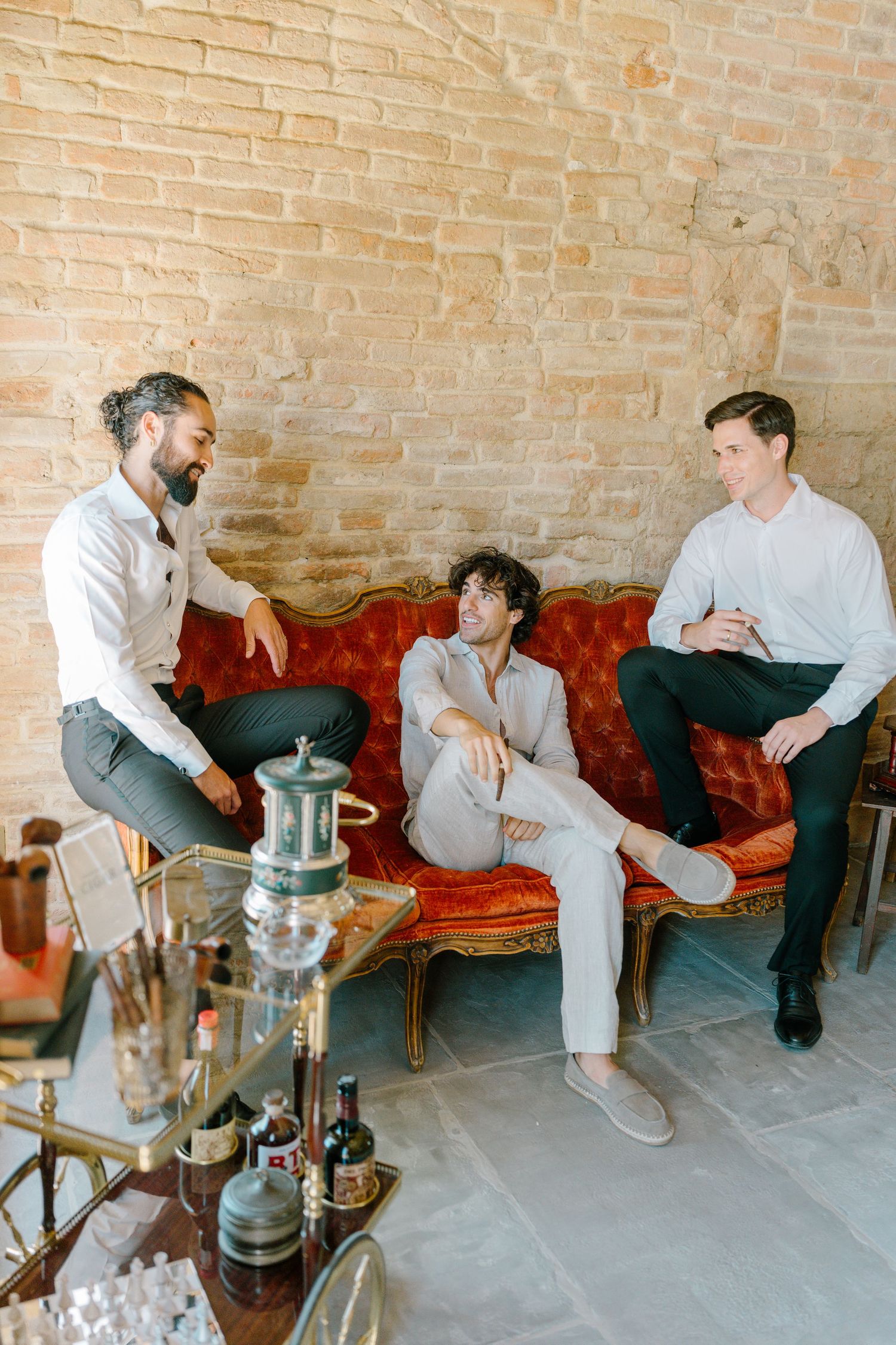 Friends lounging on red leather sofa with hookah pipes in brick-walled room.