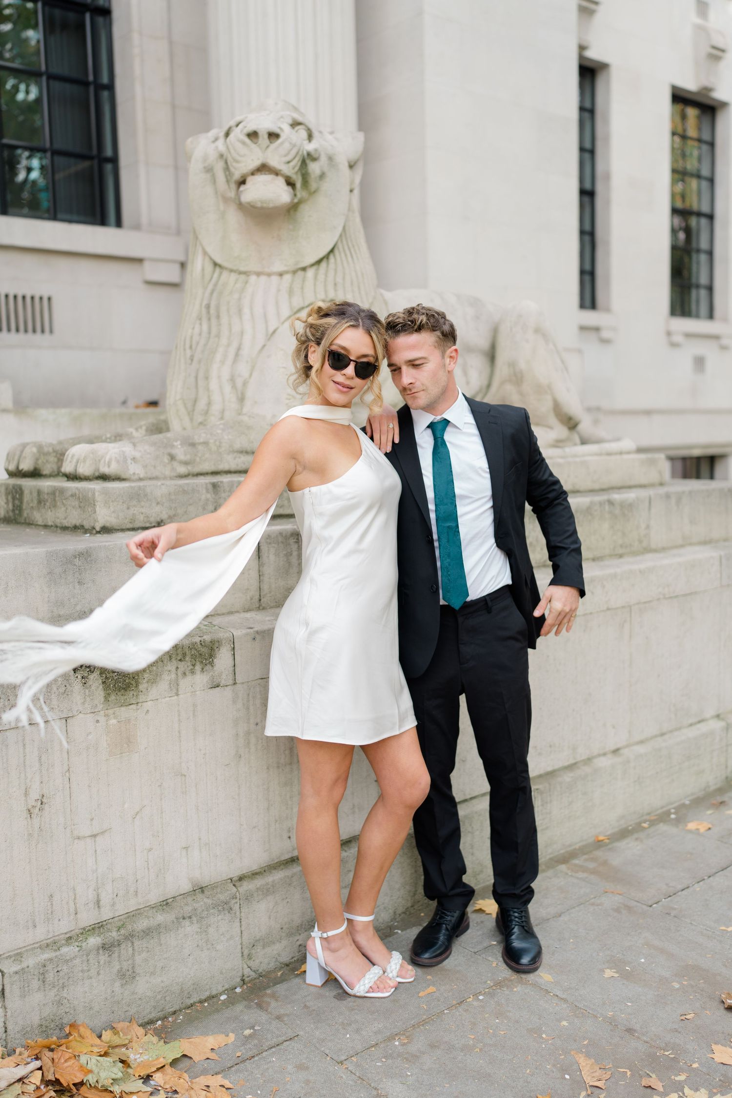 A couple poses playfully on stone steps outside a classic building.