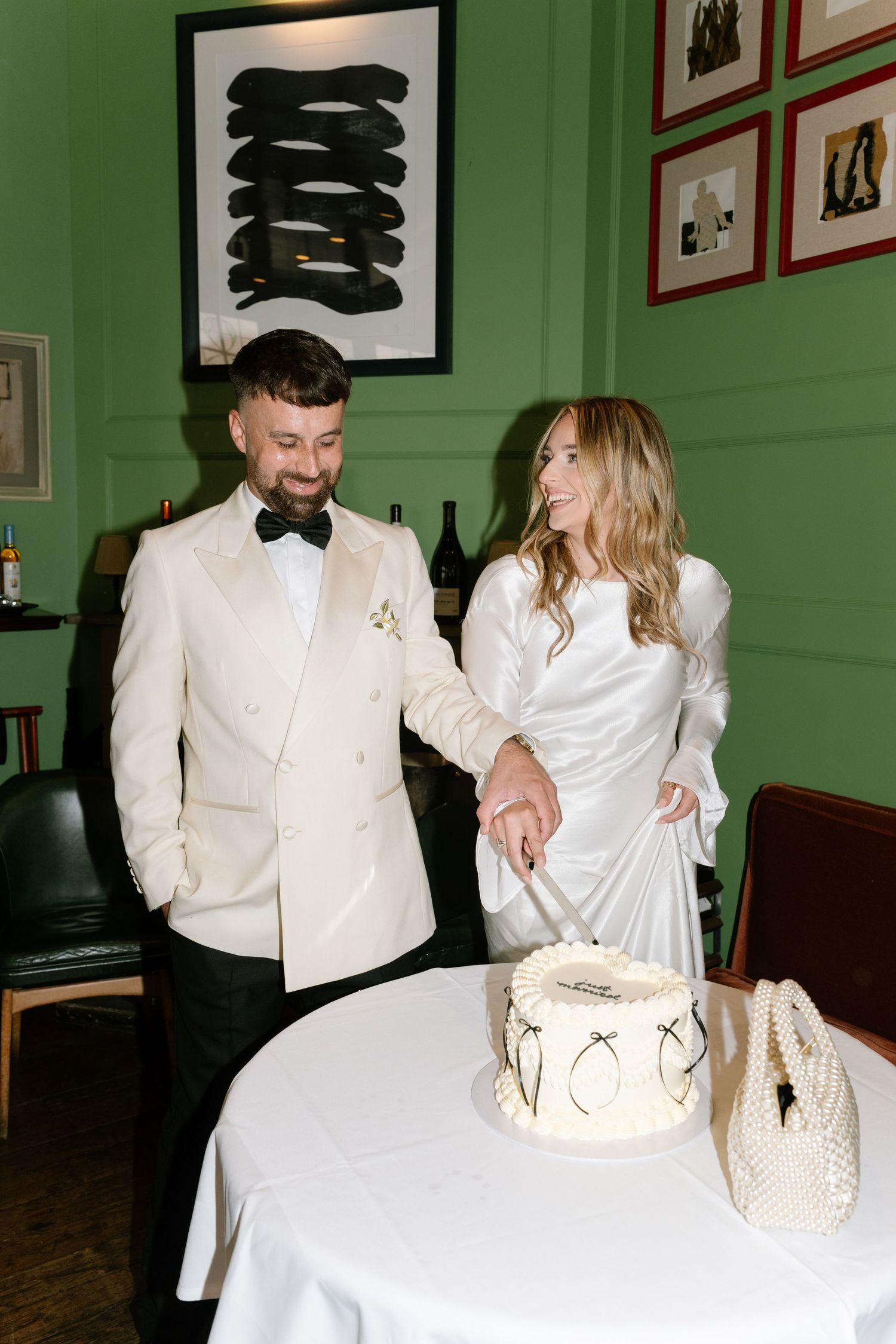 A couple cuts their minimalist wedding cake in a room with green walls and modern art.