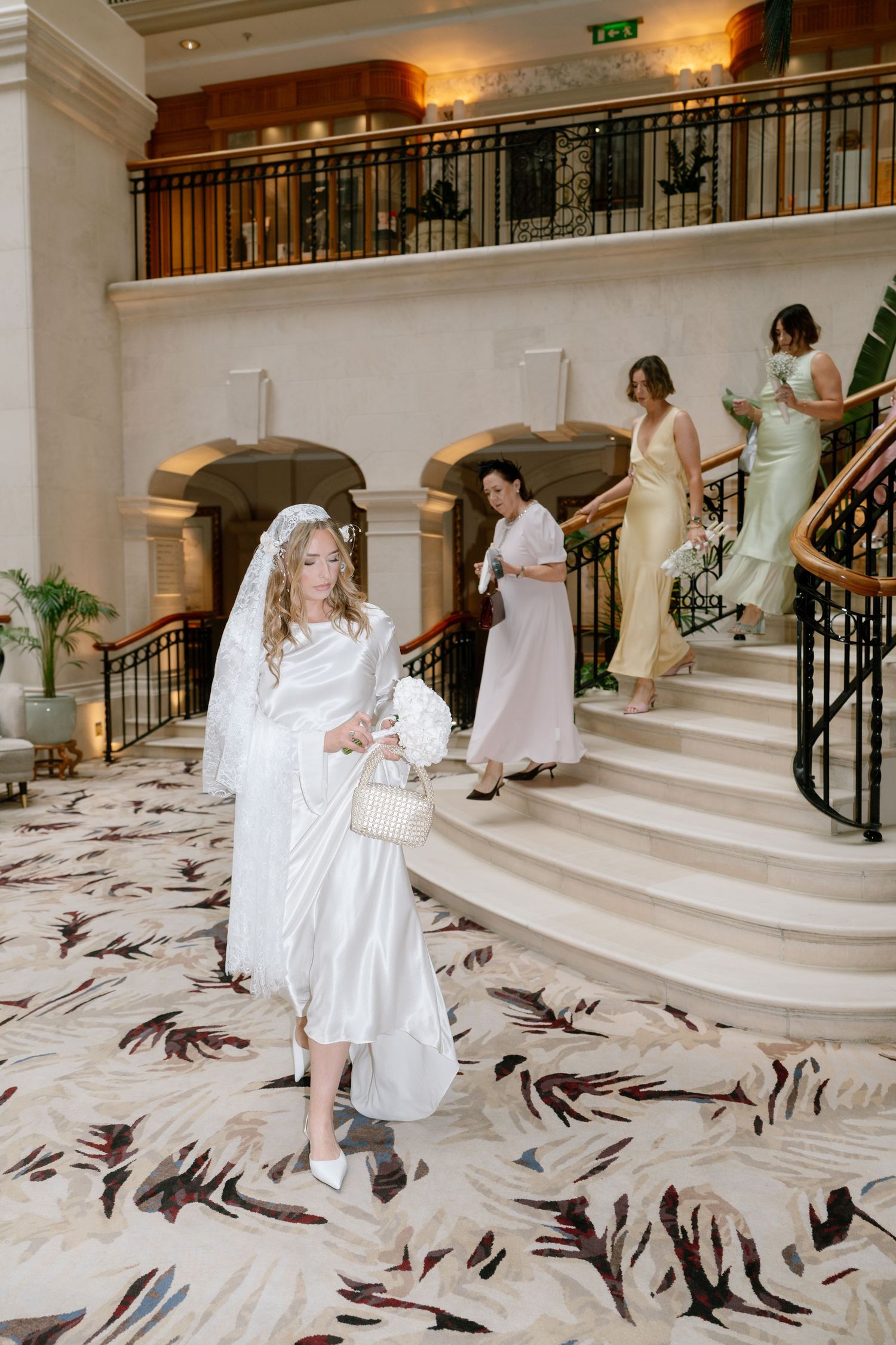 A series of photos showing a white dress descending elegant marble stairs decorated with scattered feathers.