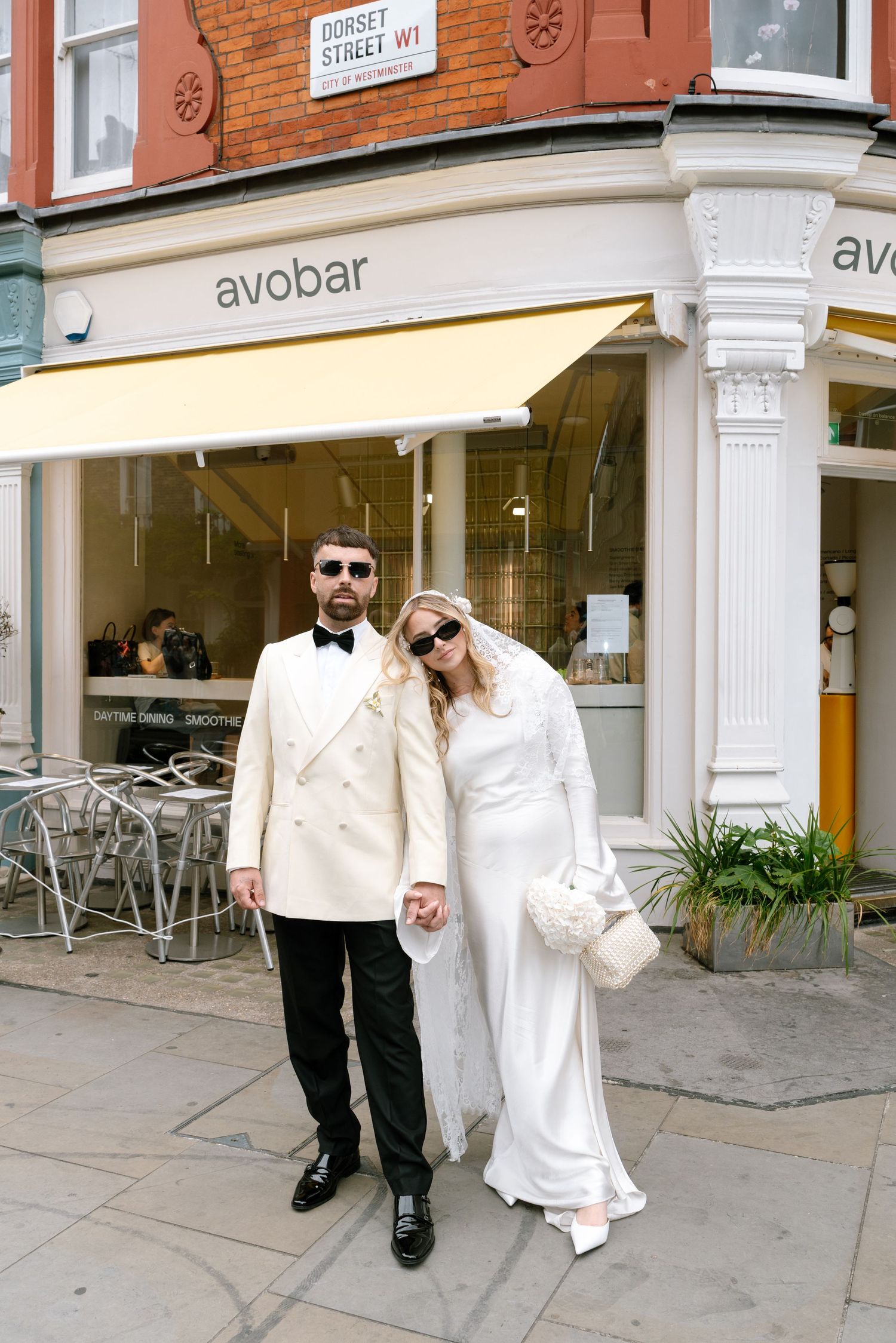Wedding couple posing outside Avobar cafe with cream and white attire.