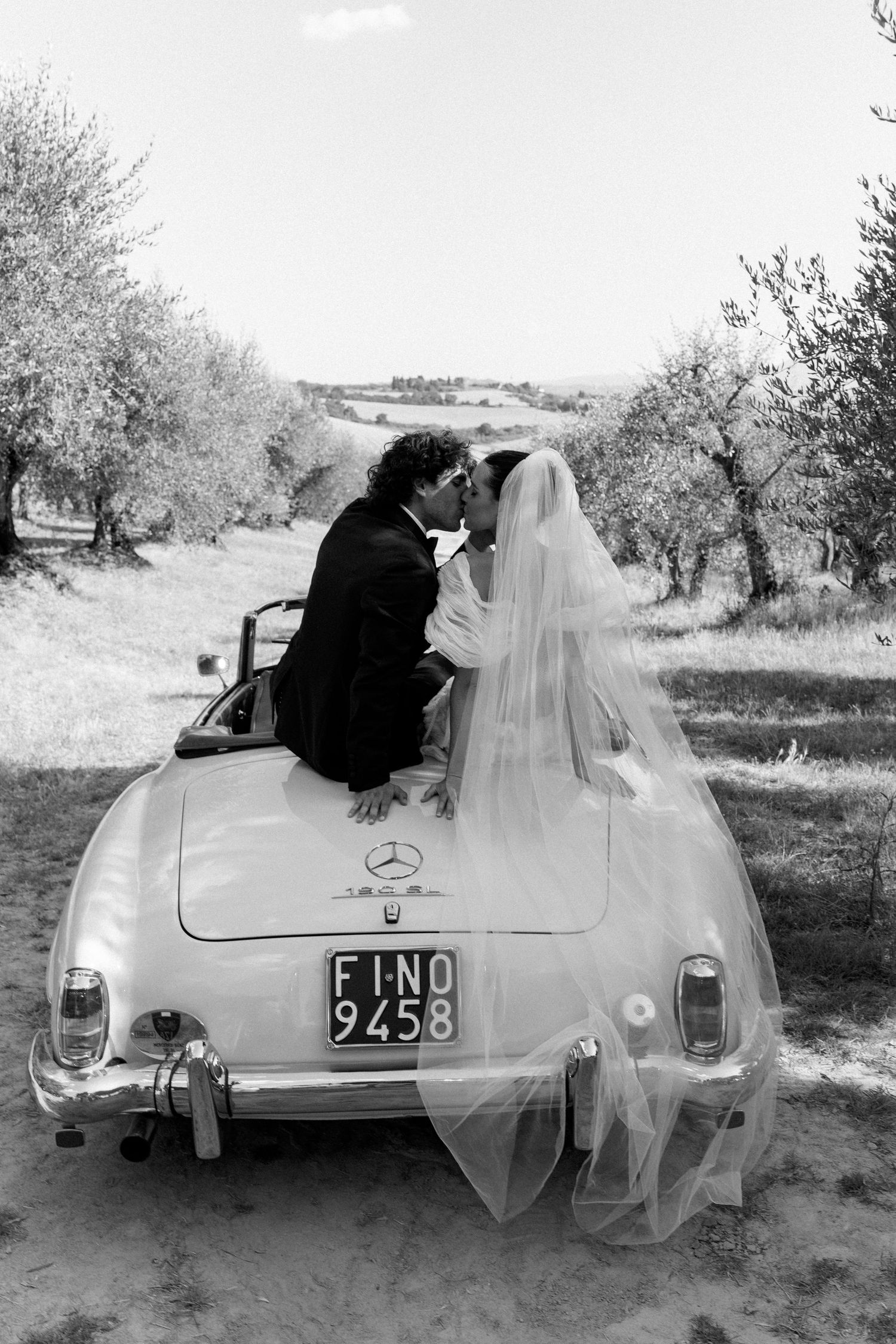 A classic Mercedes convertible decorated for a wedding with flowing white fabric.