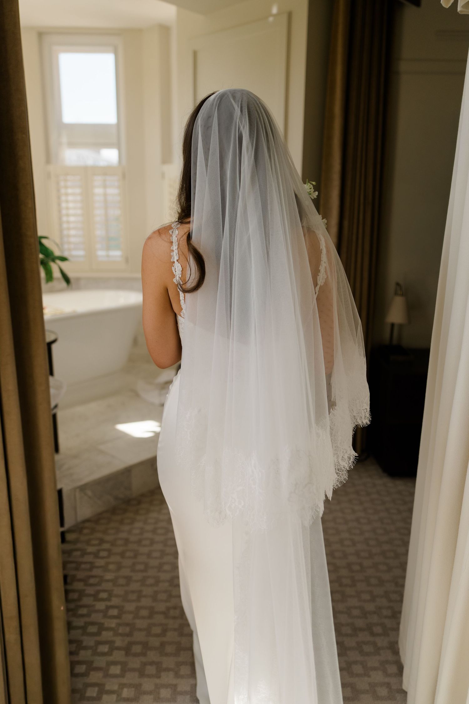 Back view of bride in fitted white lace wedding dress with long cathedral veil in mirror.