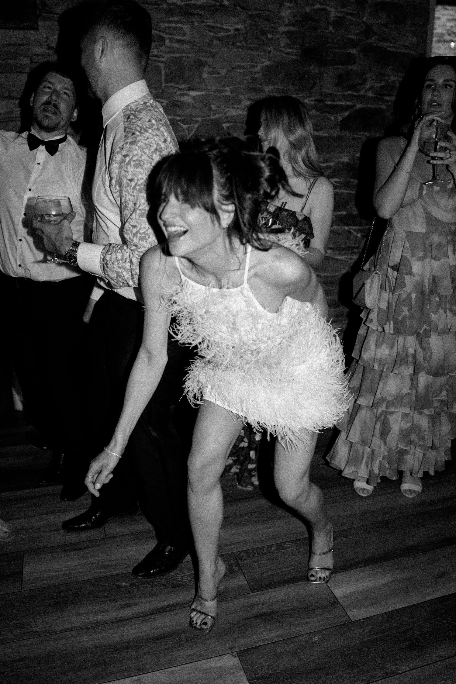 Black and white photo of dancers in formal attire showing energetic dance moves on a wooden floor.