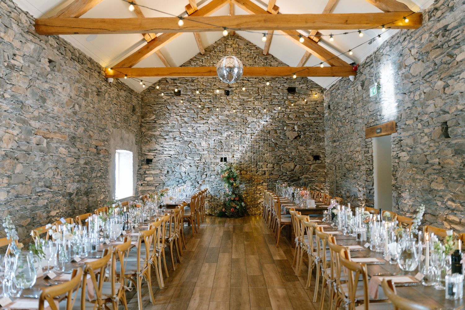 Elegant wedding reception setup in rustic stone barn with exposed wooden beams.