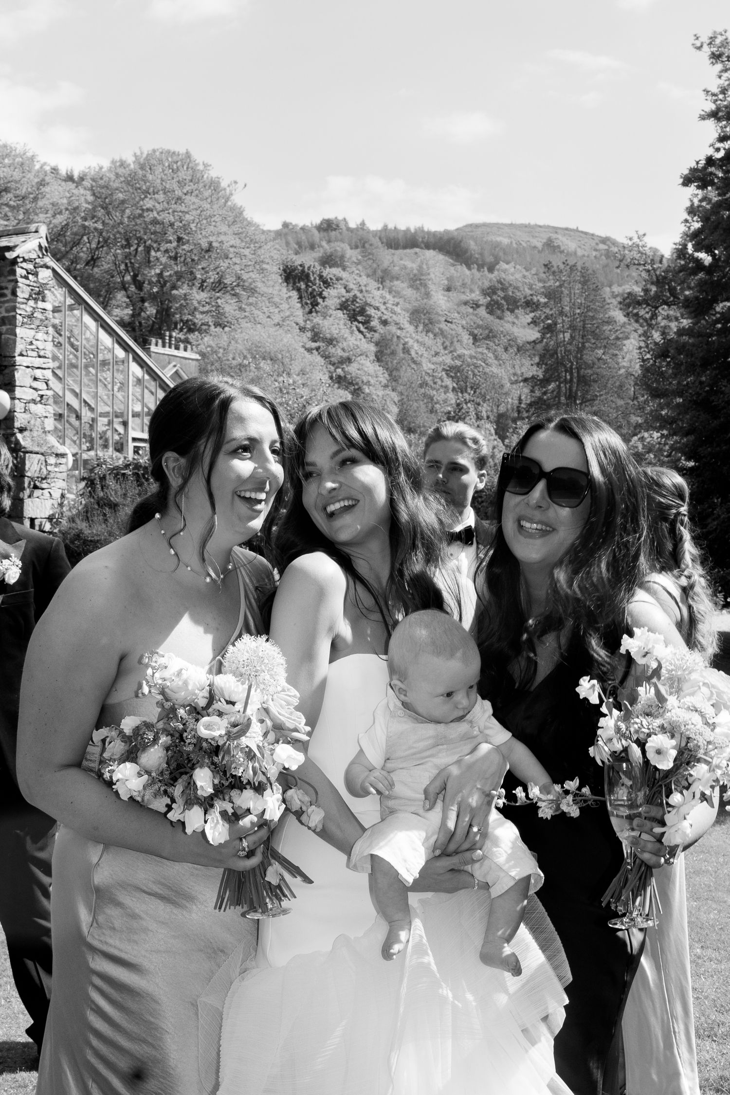 Black and white portrait of wedding party with baby outdoors against mountain backdrop.