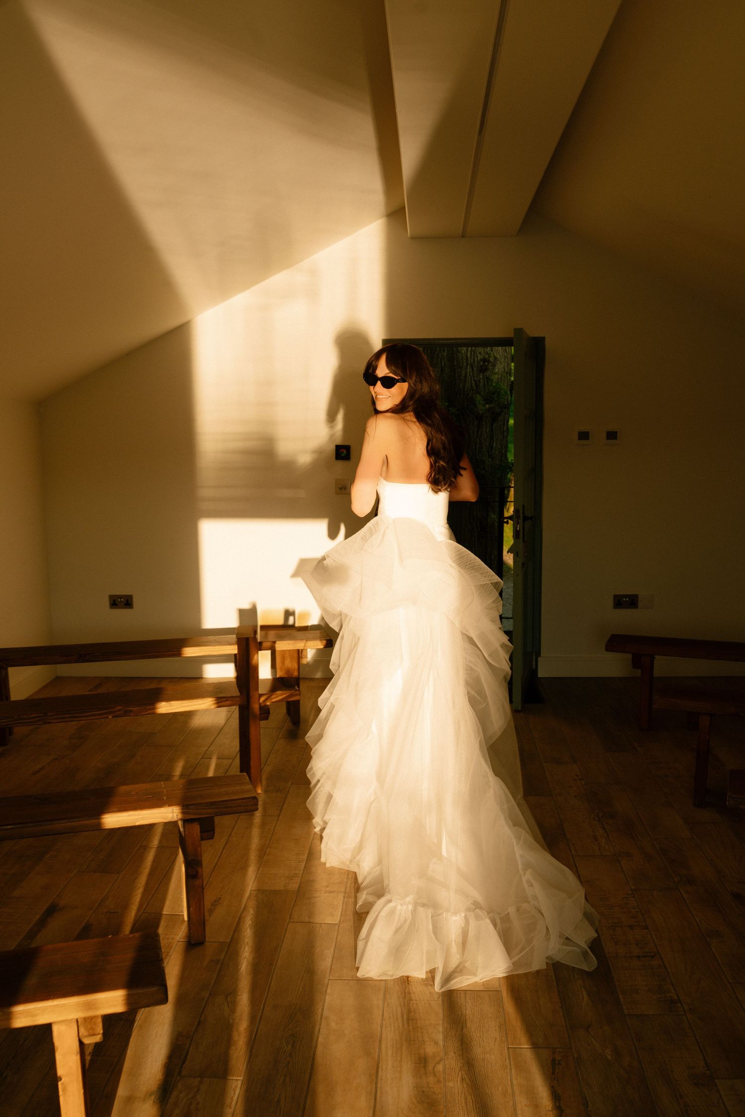 Sunlight streams through windows illuminating a flowing white wedding dress in an indoor space.