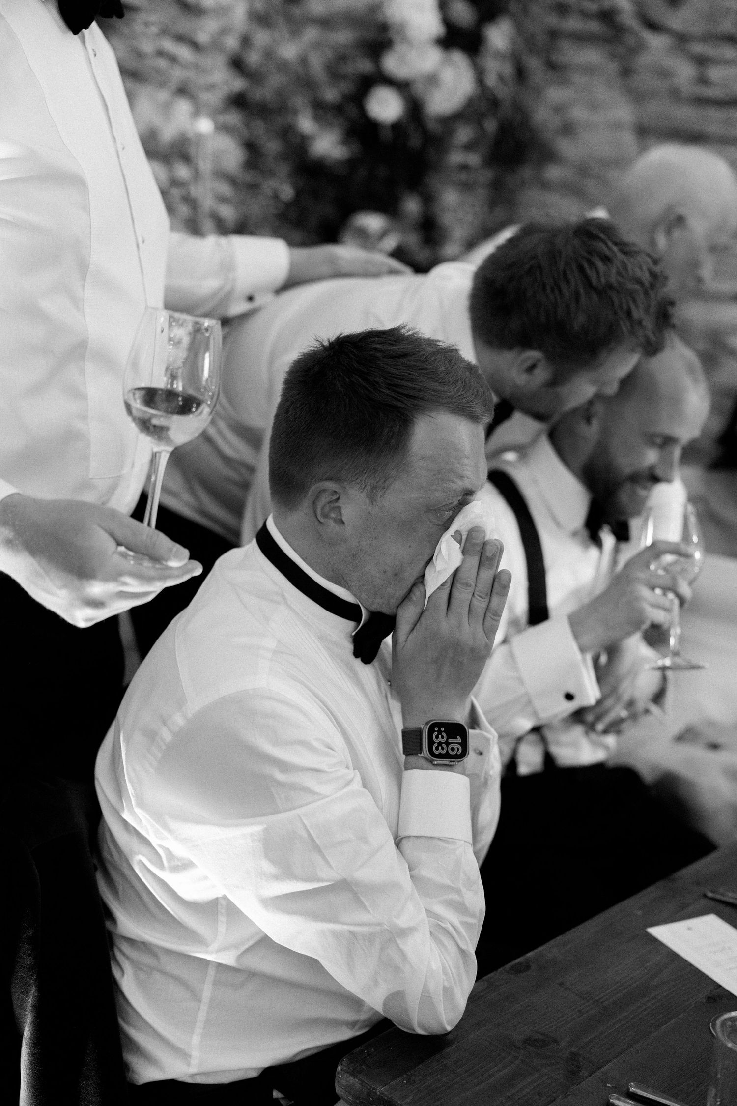 Wedding party members in white shirts and black bowties seated at a reception table.
