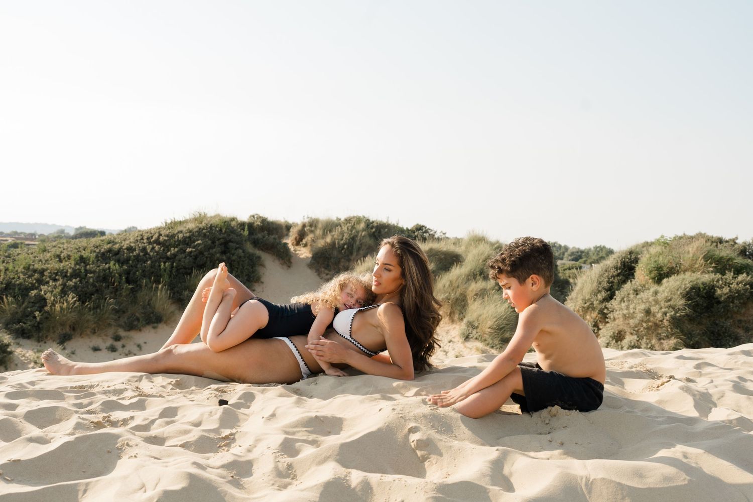 People lounging on sandy beach dunes during a sunny afternoon.