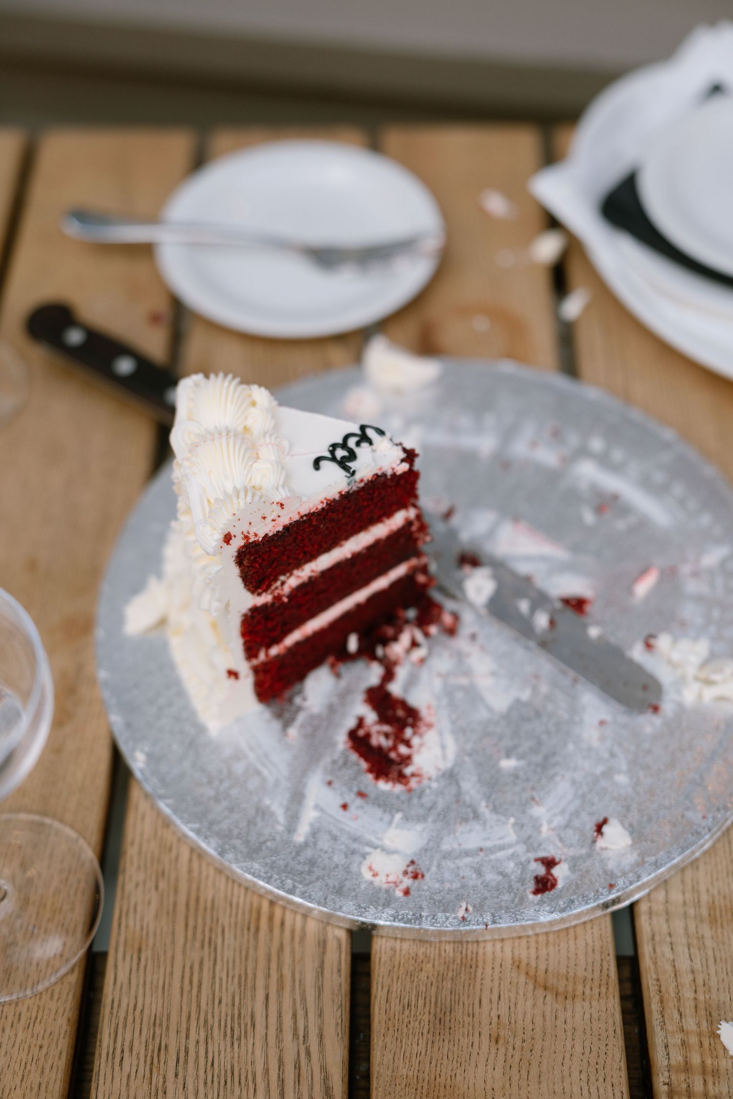 Slices of red velvet cake with white frosting on silver plates at a wedding reception.