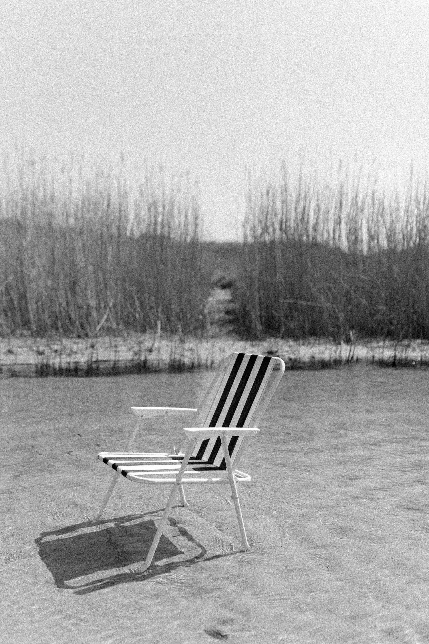 A black and white photo of a striped beach chair on an empty winter beach.
