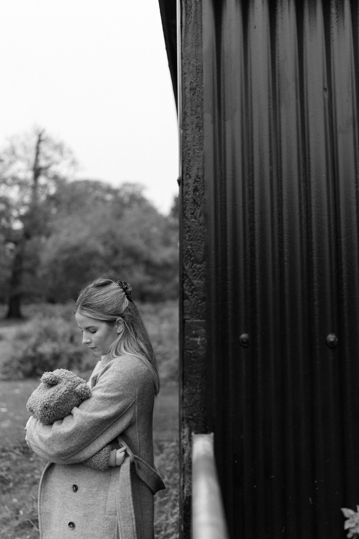 Moody black and white image showing someone standing by dark vertical bars.