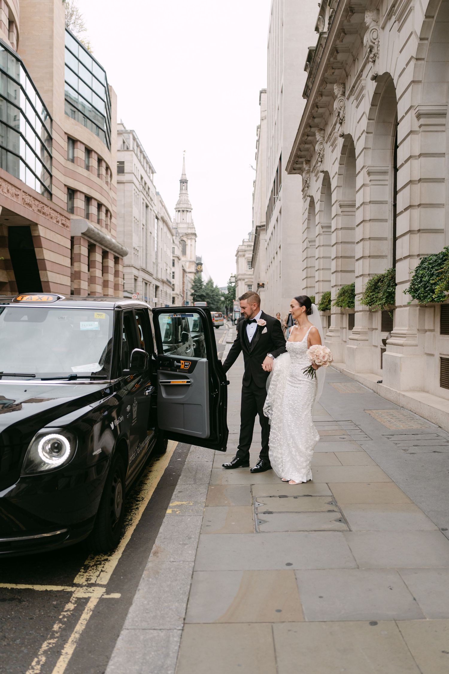 Wedding couple standing beside a black London taxi on an elegant city street.