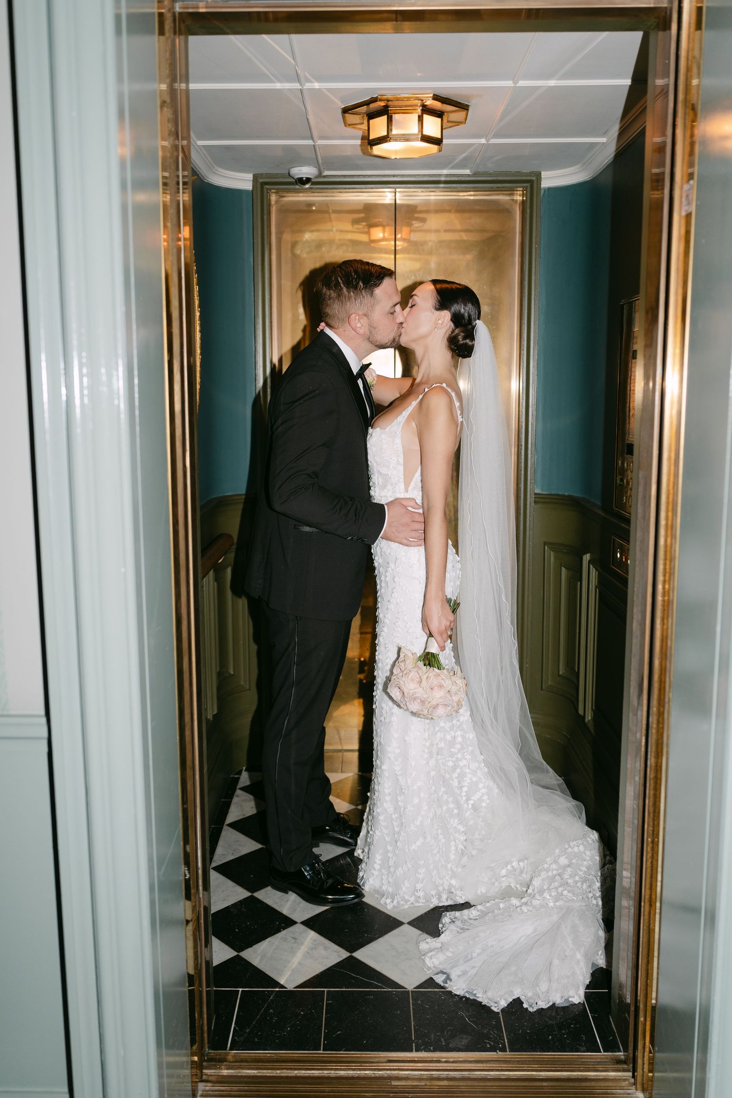 Wedding couple shares romantic kiss reflected in gold-framed mirror.