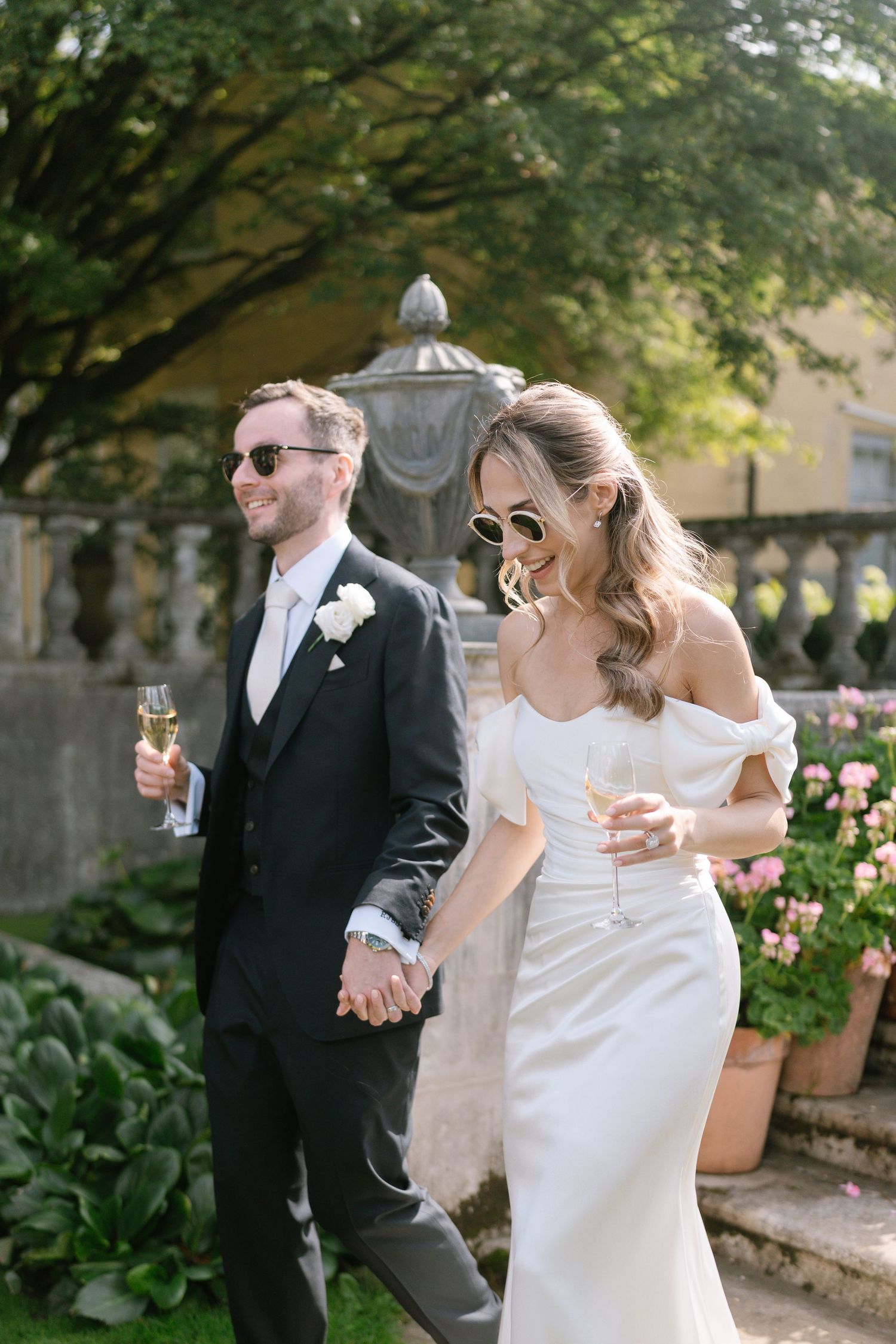Wedding couple enjoying champagne in a garden setting with stone architecture.