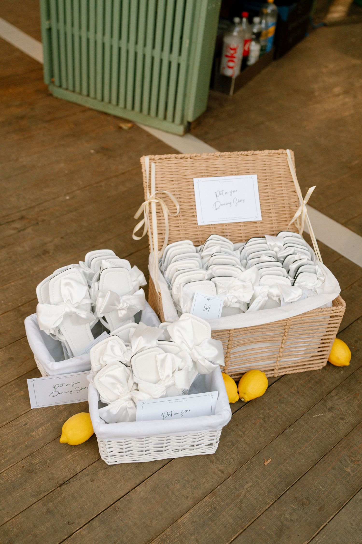 Wicker baskets filled with white favor packages and fresh lemons on wooden floor.