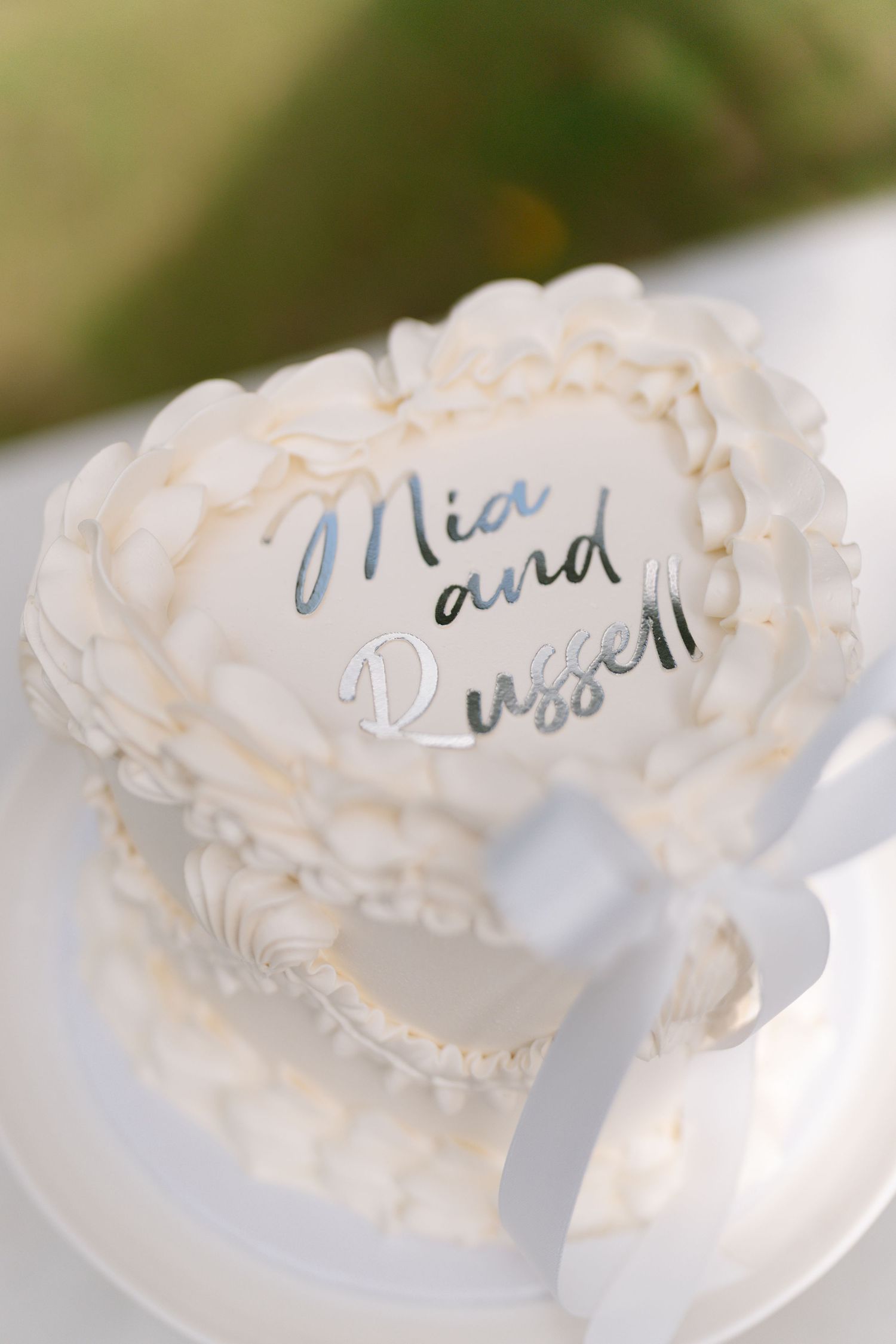Close-up of elegant white wedding cake with decorative piping and text.