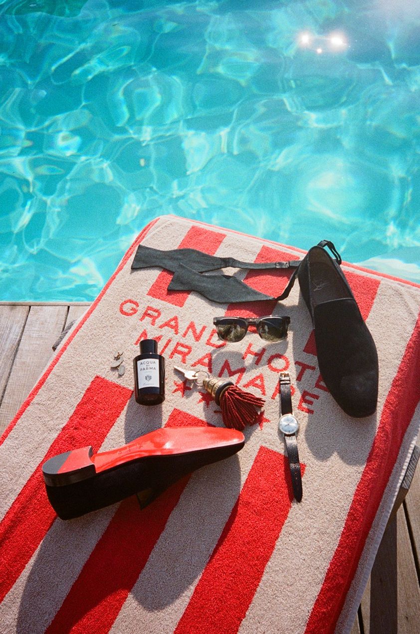 Red striped Grand Hotel Miramare towel by pool with loafers, sunglasses, watch, and cologne.