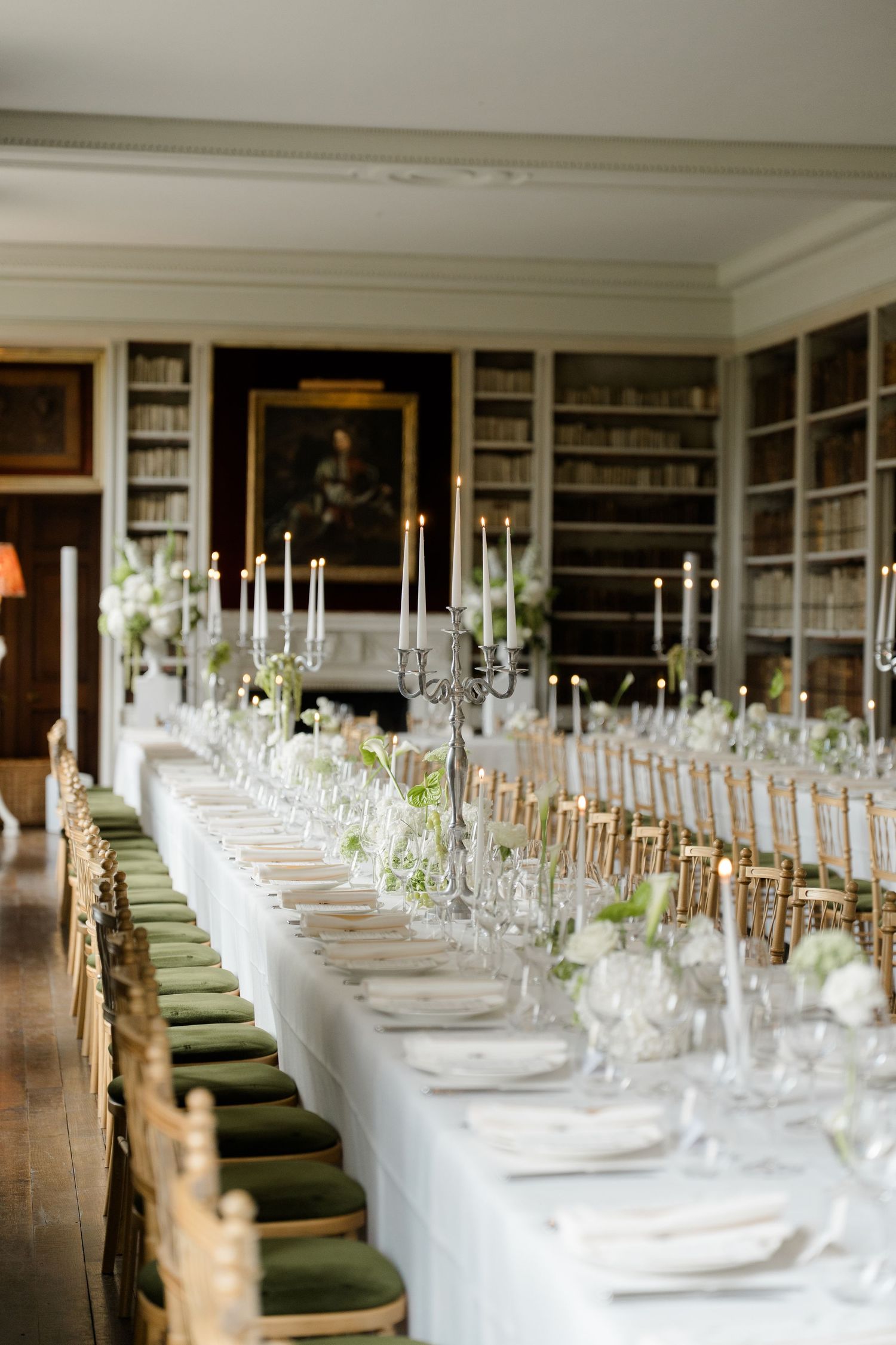 Elegant wedding reception table with candelabras, white florals, and gold chairs in a library venue.
