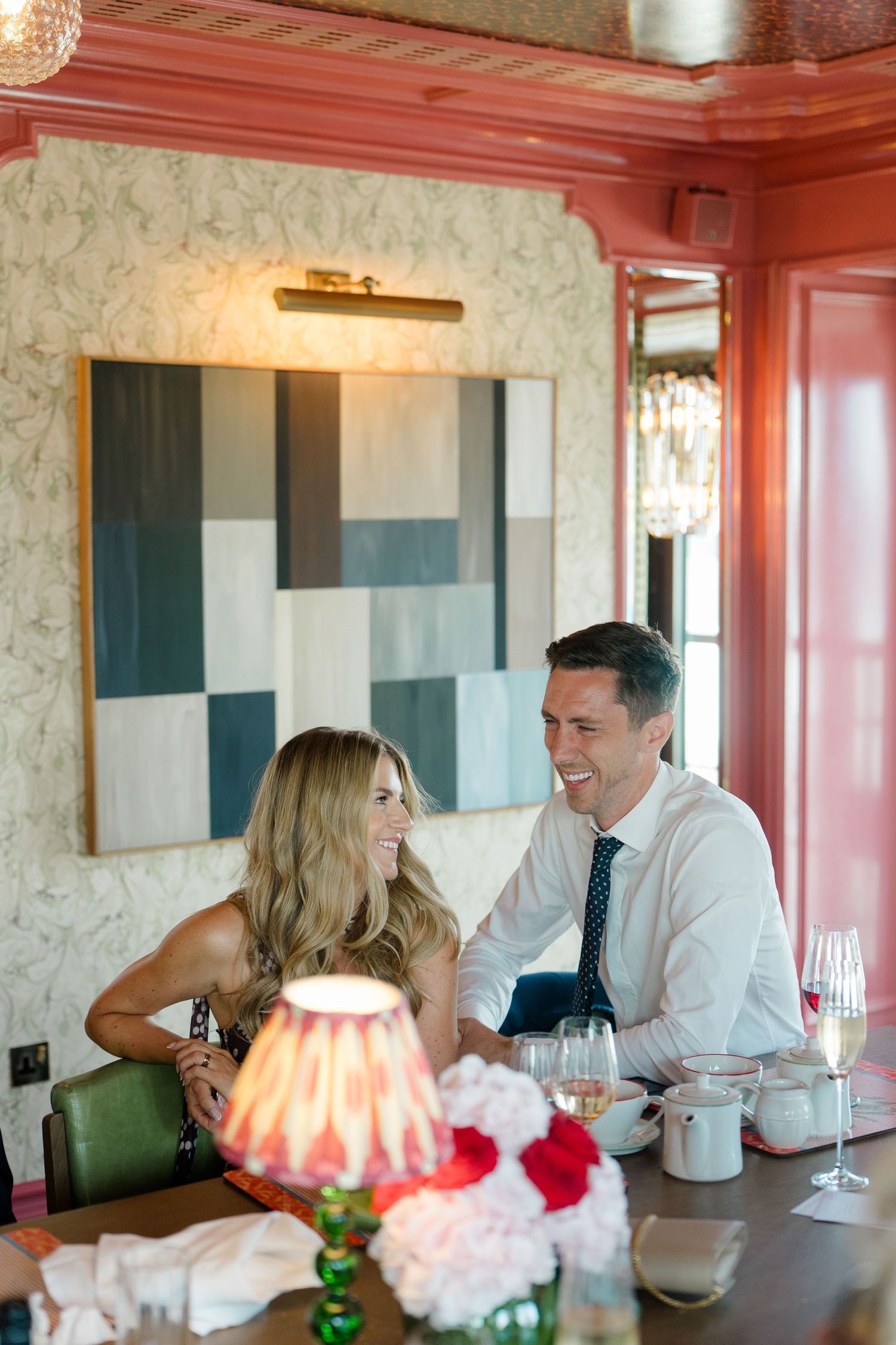Smiling couple enjoying wedding reception dinner in elegant red-trimmed dining room with floral centerpiece.