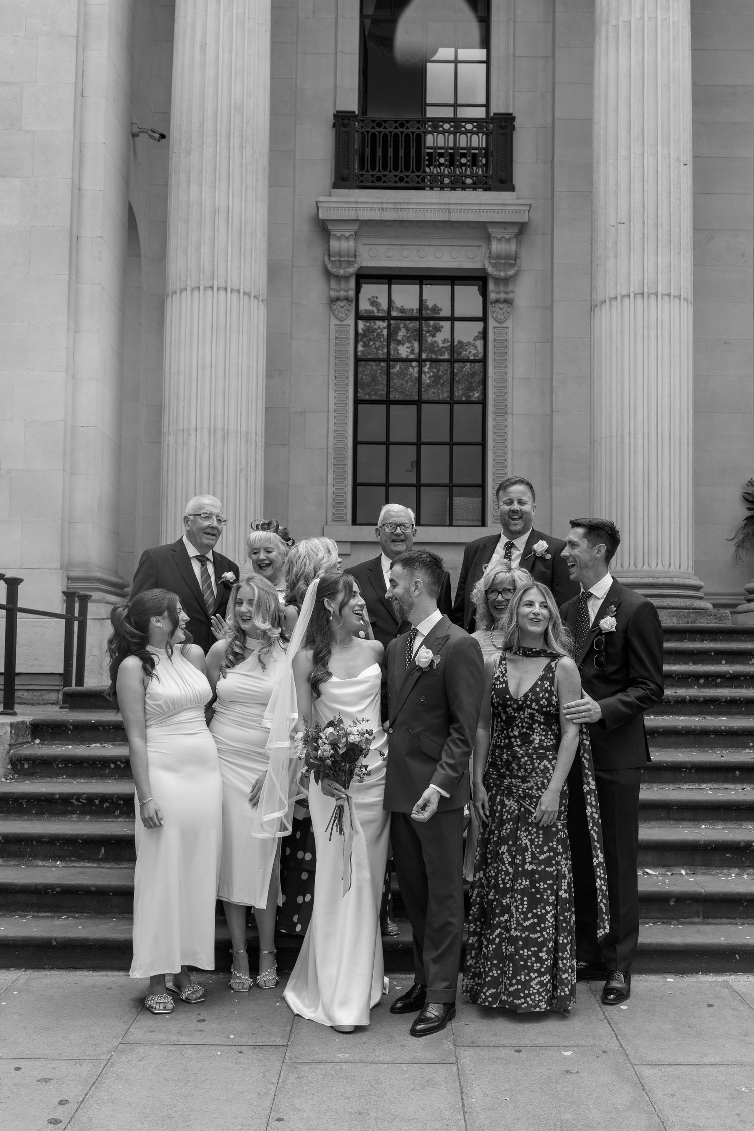 Black and white group portrait of bride, groom and family on steps of grand neoclassical building.