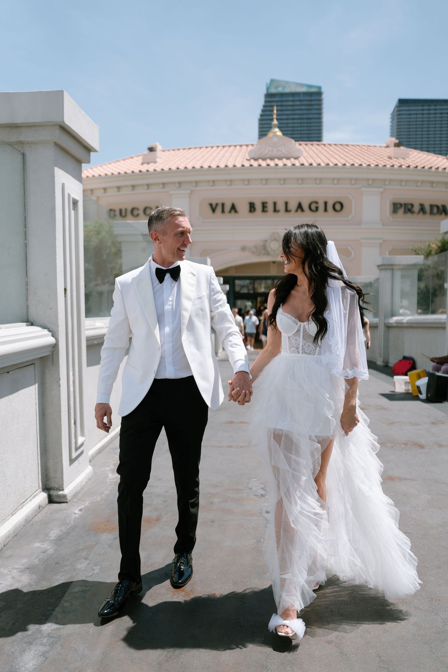 Wedding couple walks hand in hand outside Caesars Palace in Las Vegas wearing white formal attire.