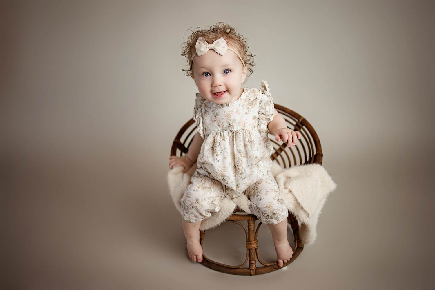 Baby wearing white lace dress sitting in antique wooden rocking chair.