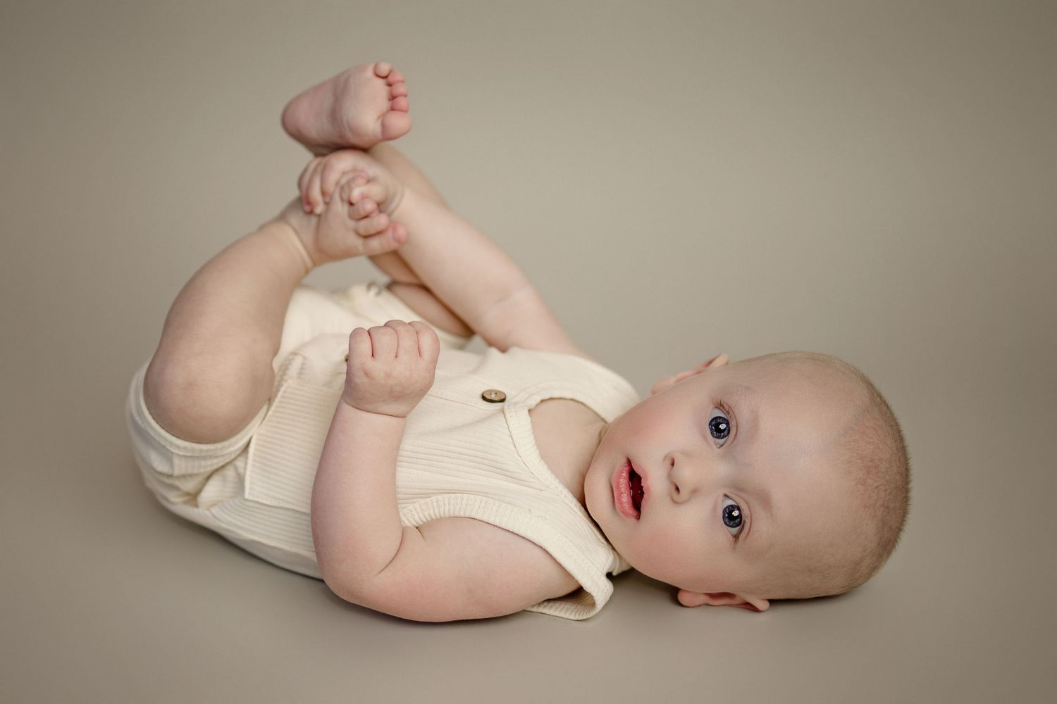 Baby in cream colored onesie lying on side in professional studio portraits.