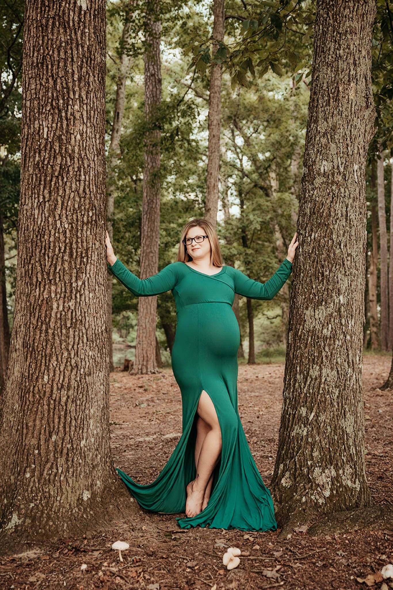 A flowing emerald green dress beautifully contrasts against a wooded forest backdrop in this artistic portrait session.
