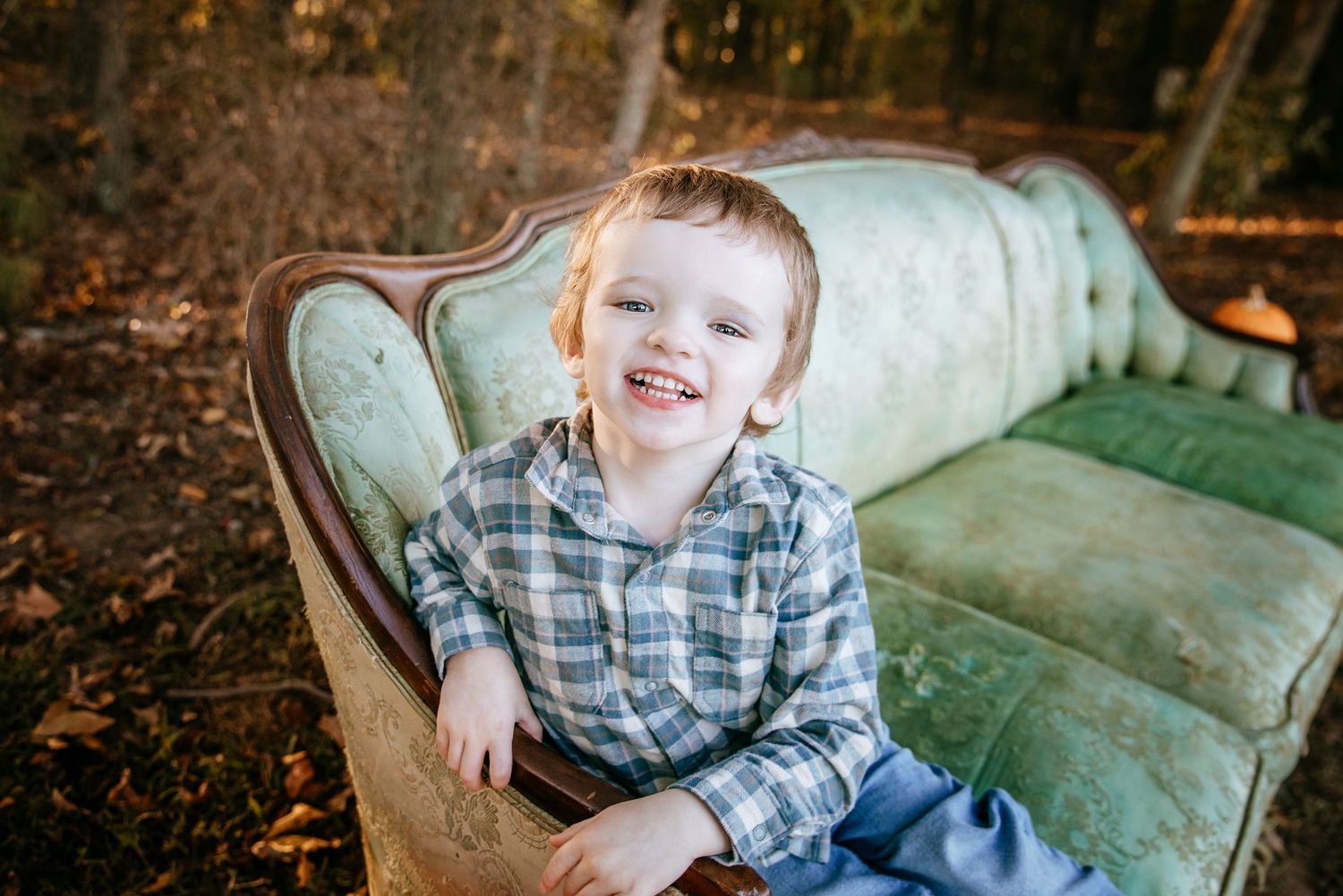 Child sitting on vintage mint green sofa outdoors in autumn setting.