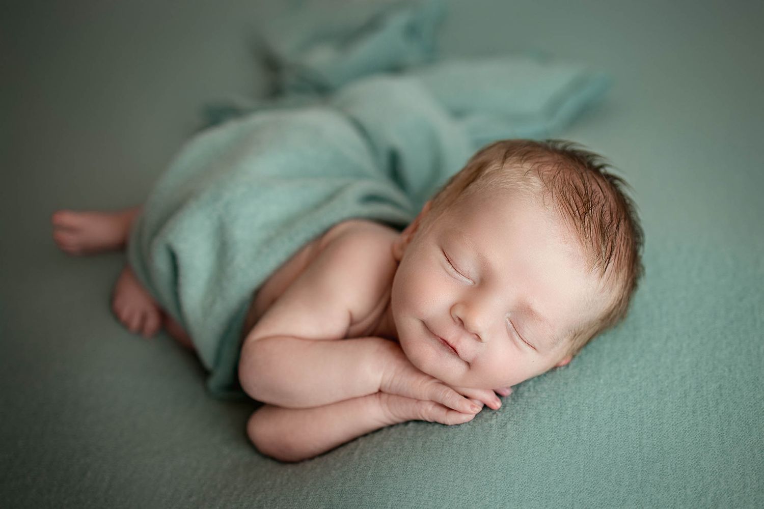 Sleeping newborn in mint green wrap on matching textured background.