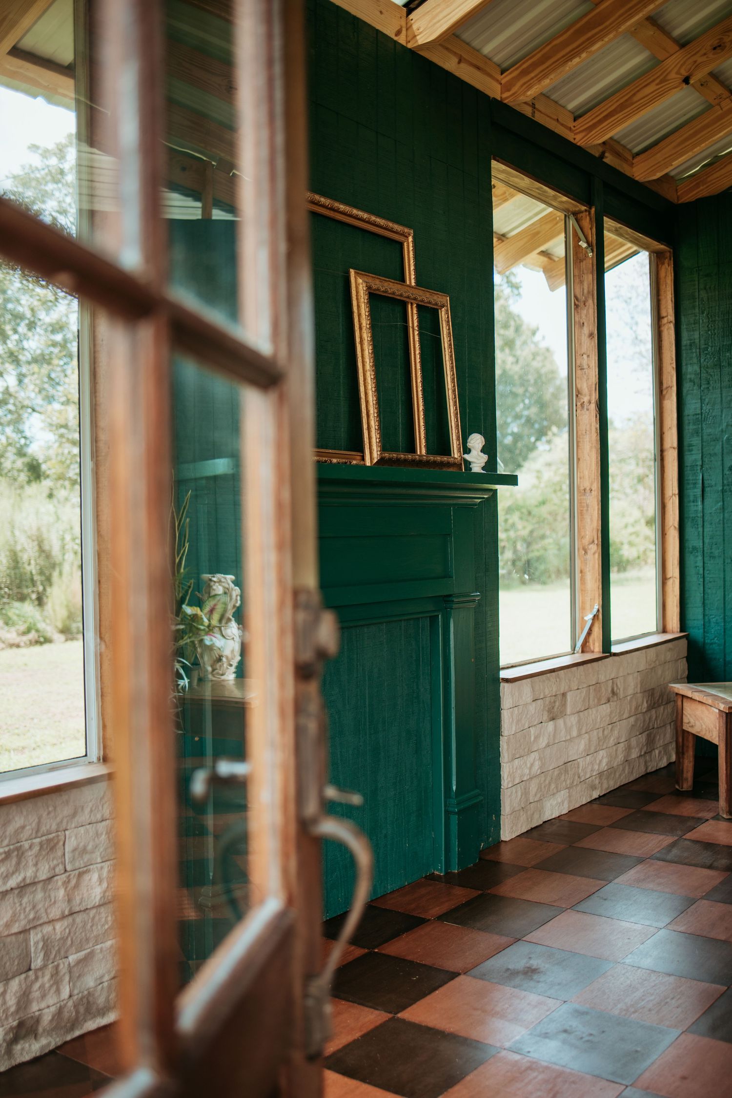 Rustic interior hallway with stone walls, deep green wood paneling, and large windows overlooking an outdoor landscape.